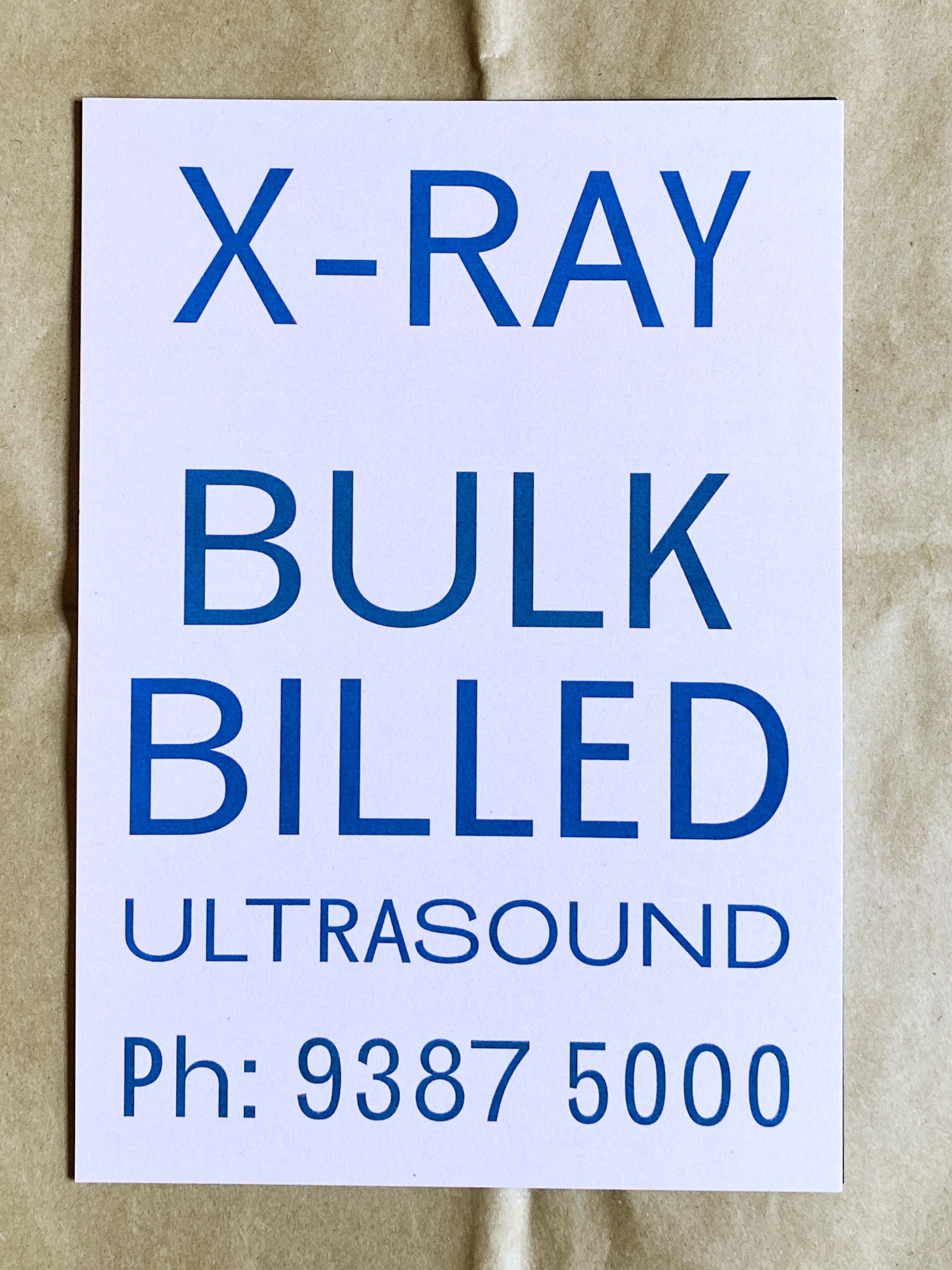 Minimalist sign with blue text reading, "X-RAY BULK BILLED ULTRASOUND Ph: 9387 5000" on a plain background.