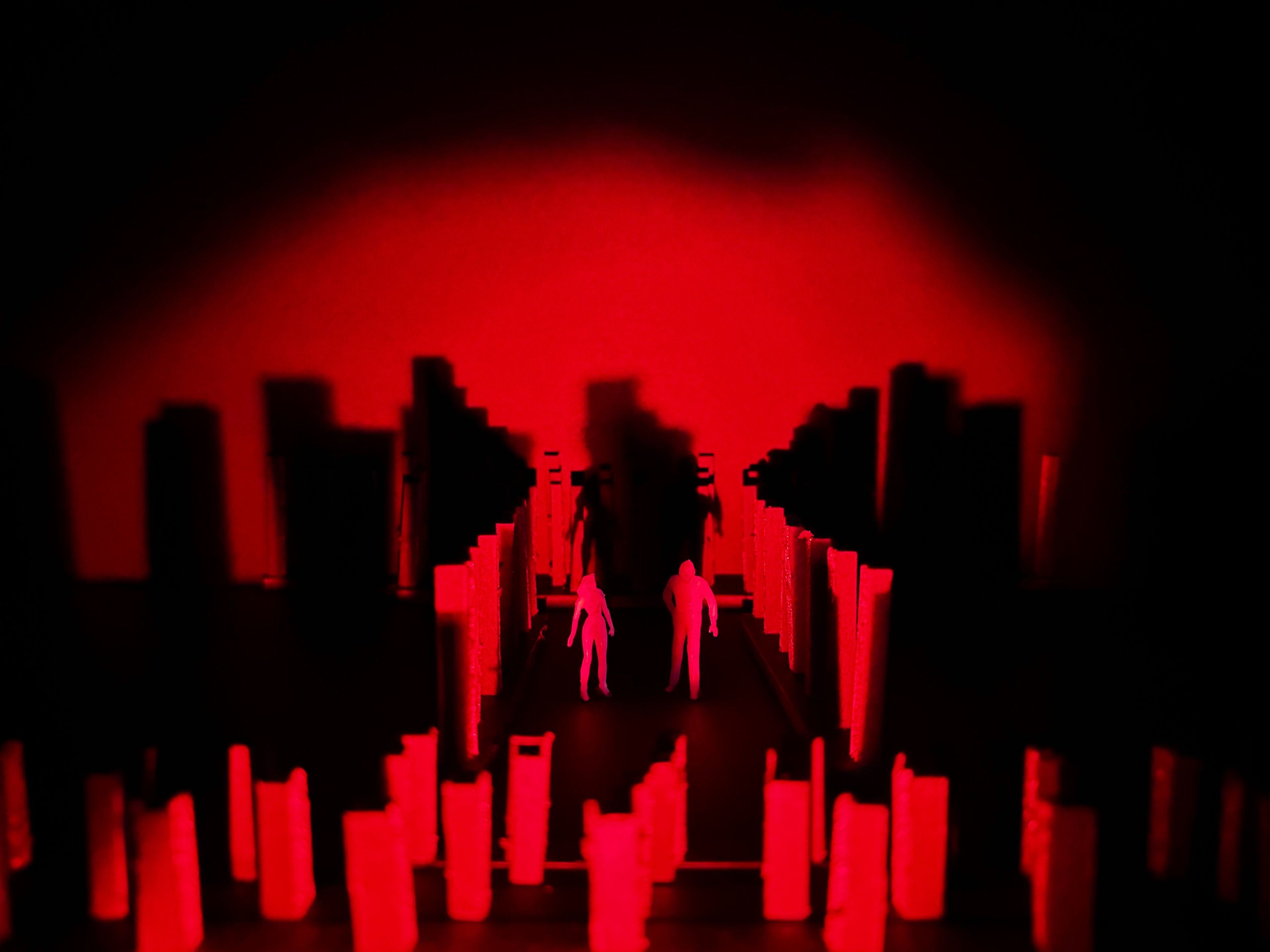 Set model with two white figures walking along a pathway between tall, red-lit structures.