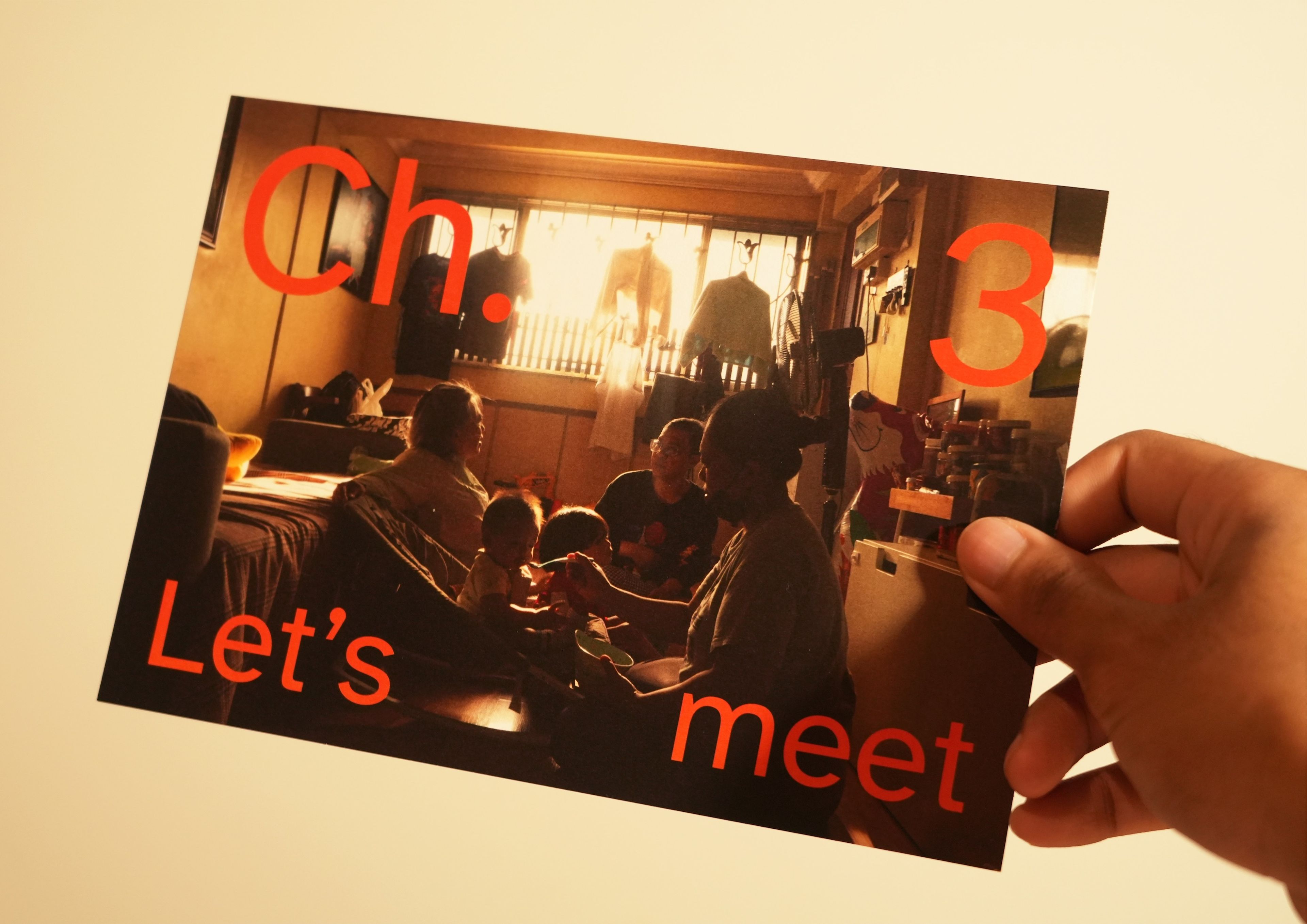 Hand holding a photograph with red text overlay reading 'Ch. 3 Let's meet'. Image shows people gathered in a warmly lit room backlit by window light, creating intimate atmospheric scene with silhouettes.