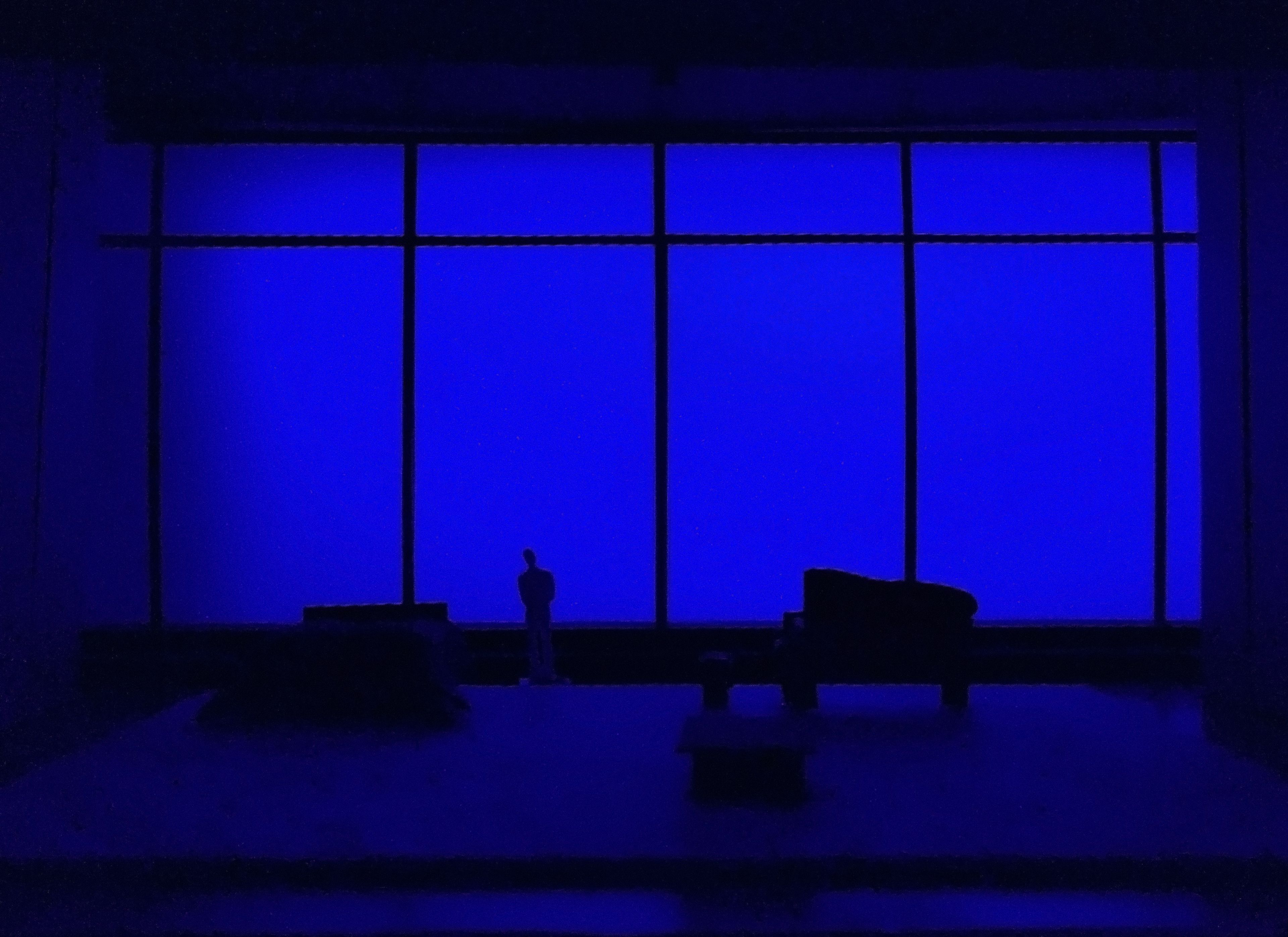 Scale model of a set design with a deep blue backdrop, silhouetting a lone figure on stage.