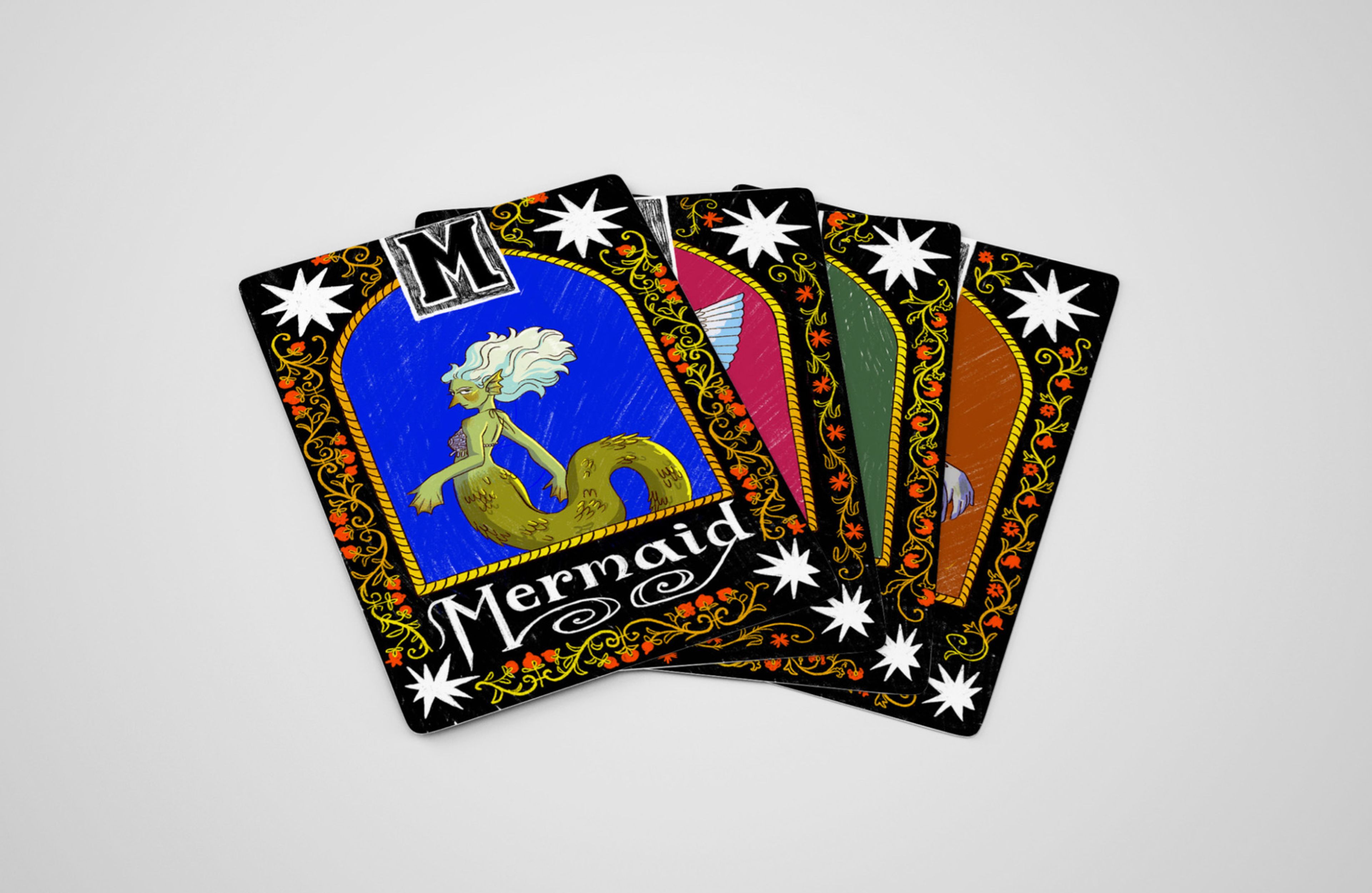 A stack of illustrated cards lies fanned out on a white surface. The top card features a "Mermaid" with a green tail and flowing white hair, set against a blue background with ornate floral borders