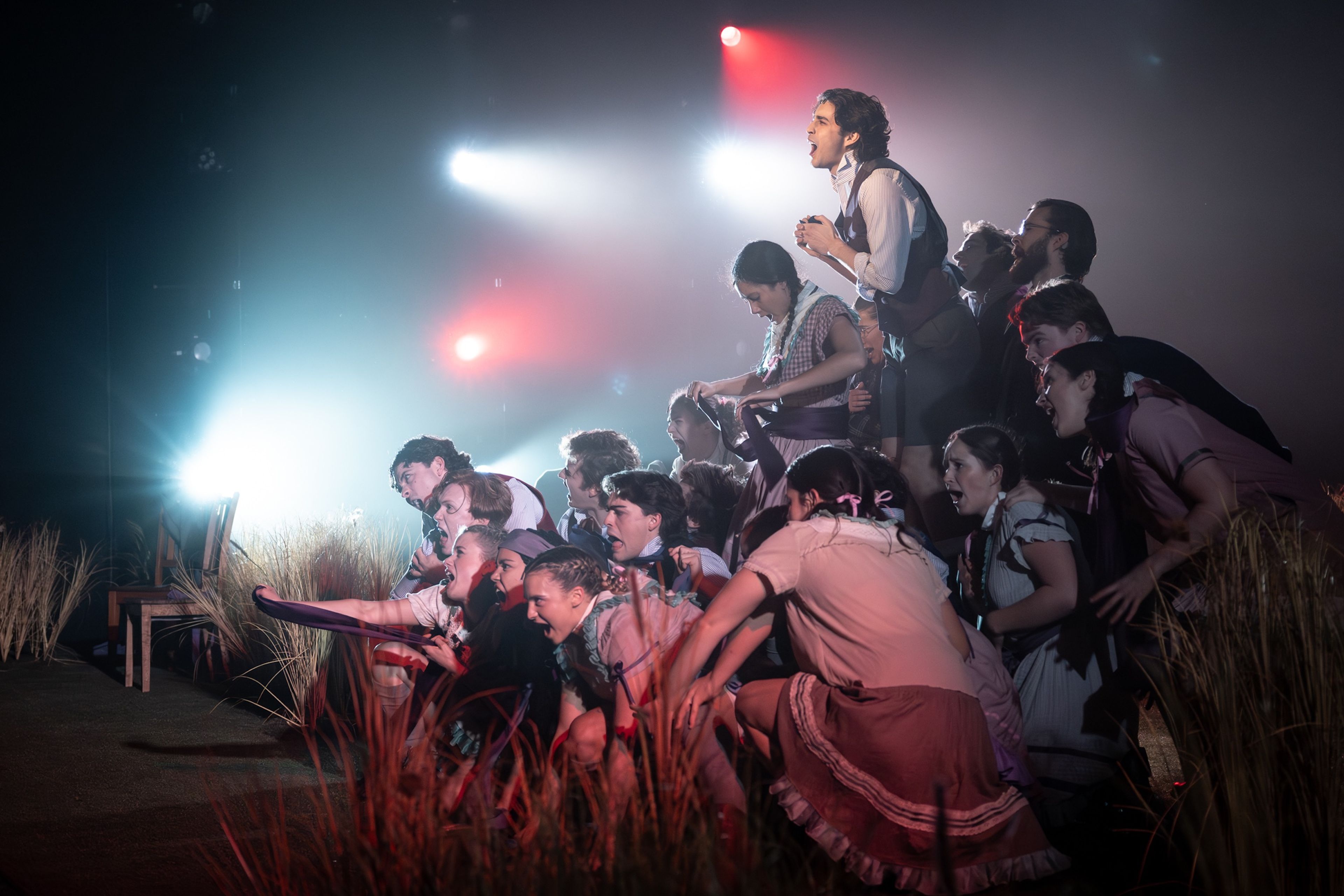 A large ensemble cast crouches and leans forward, dramatically lit against a hazy, atmospheric backdrop with red and blue lighting.