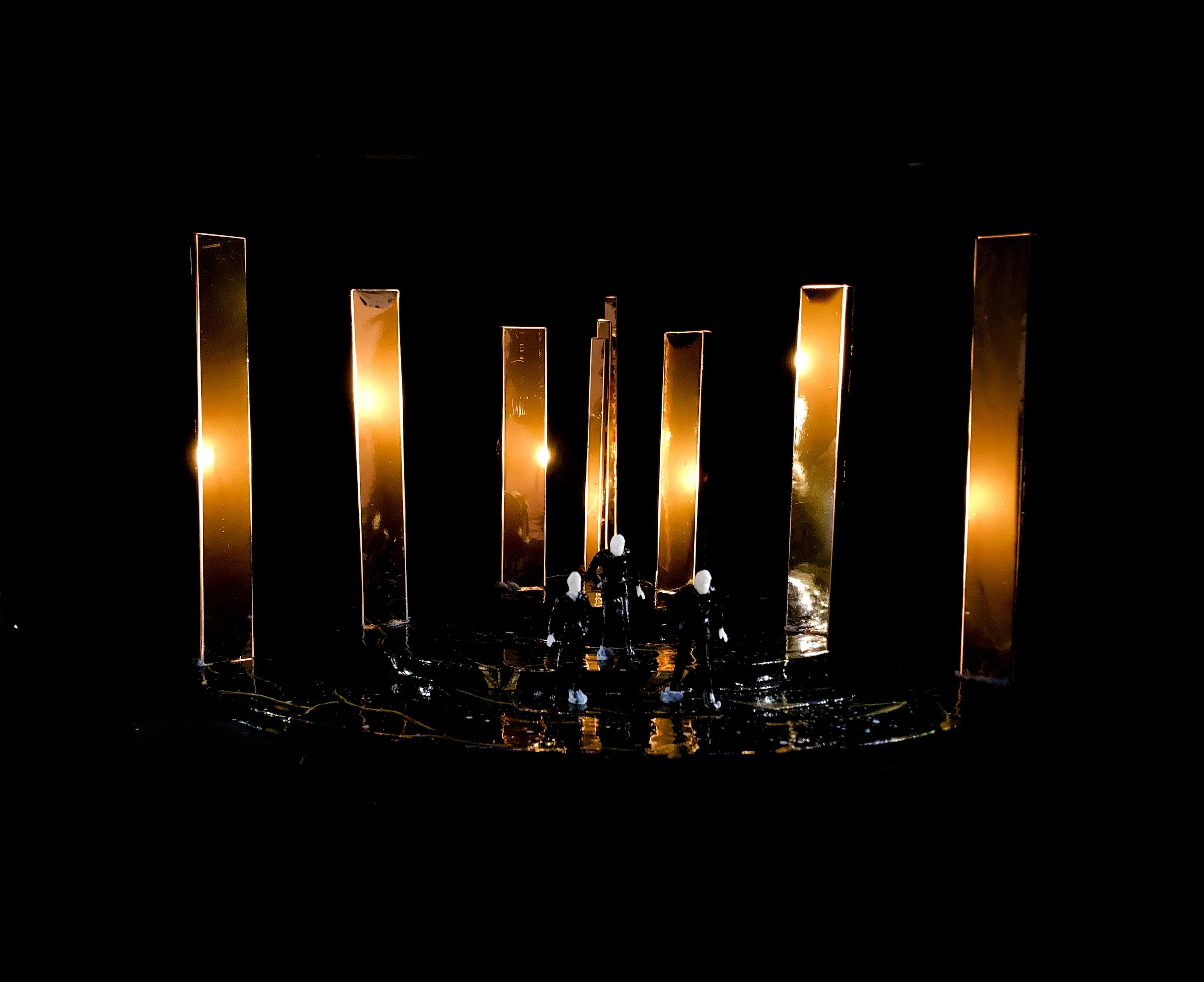 Set model for Act 5, Scene 3, featuring tall illuminated golden columns with miniature figures on a dark stage.