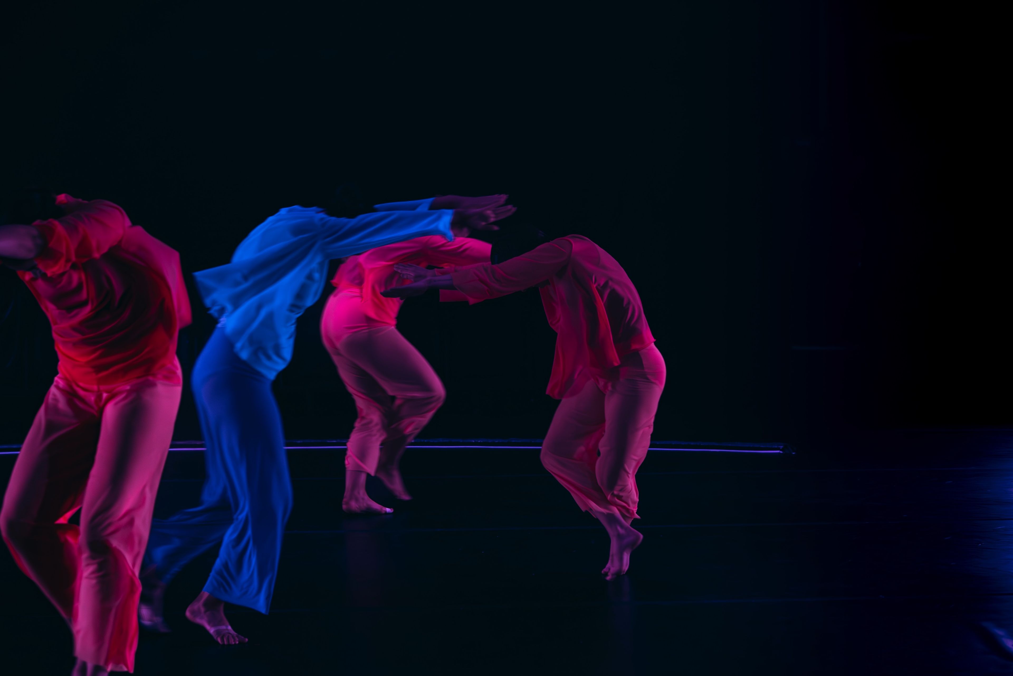 Dance performance photograph capturing dancers in pink and blue costumes, creating a flowing arc of motion.