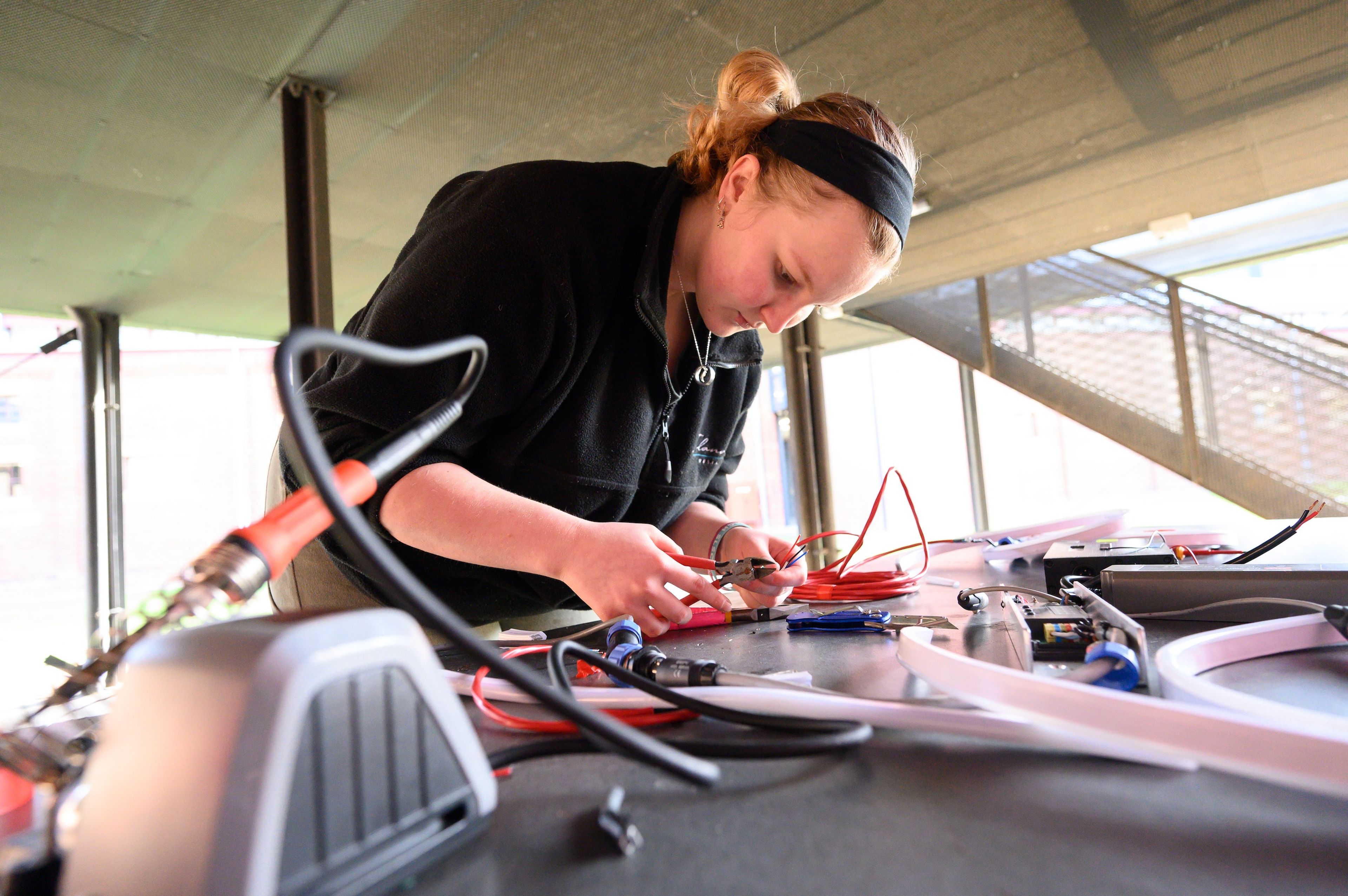 Close-up of a crew member working with electrical wires and tools on a table, focused on a technical task with various cables and equipment around.