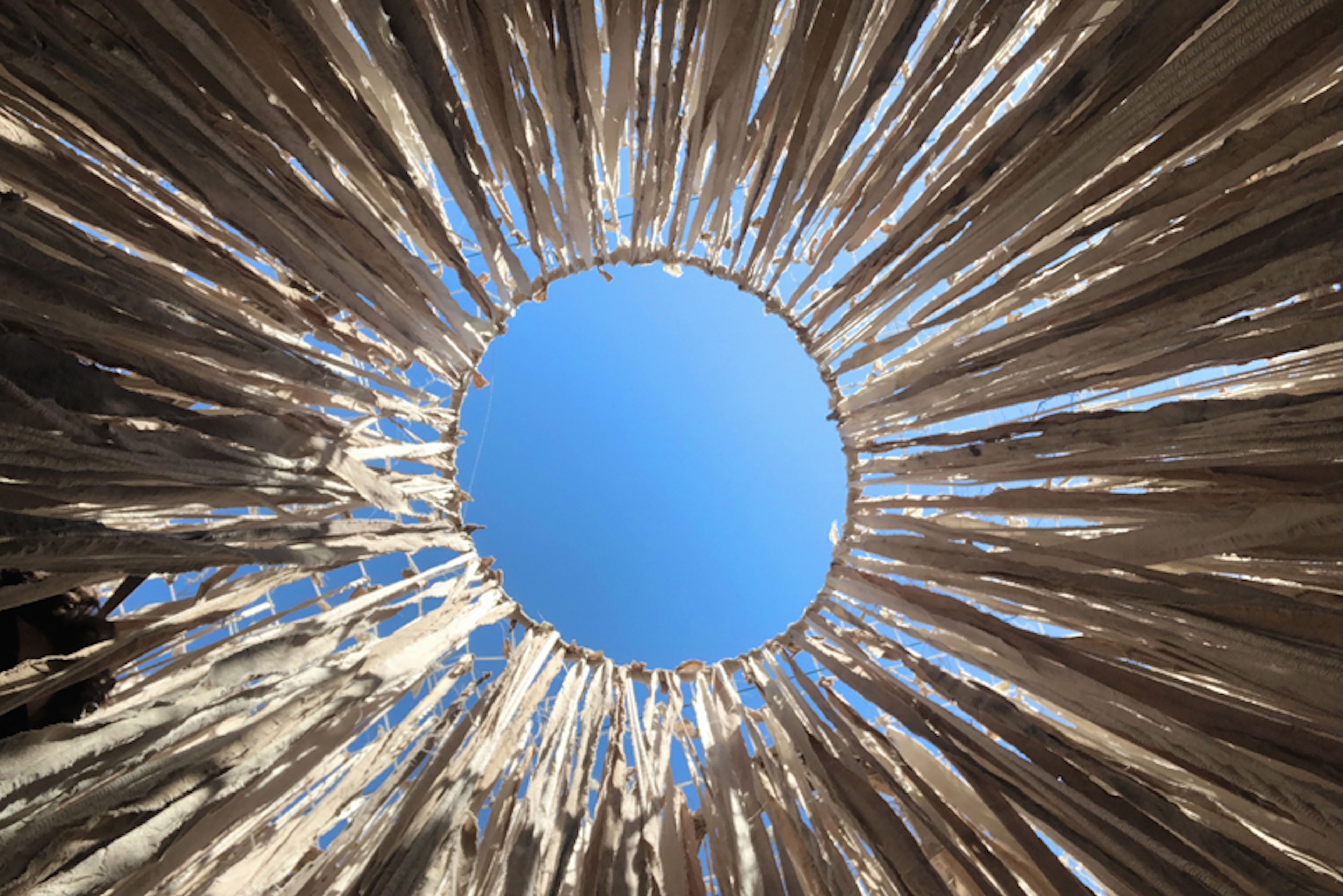 Set design photograph showing a circular opening in a fabric ceiling, creating a dramatic sunburst effect against bright blue sky