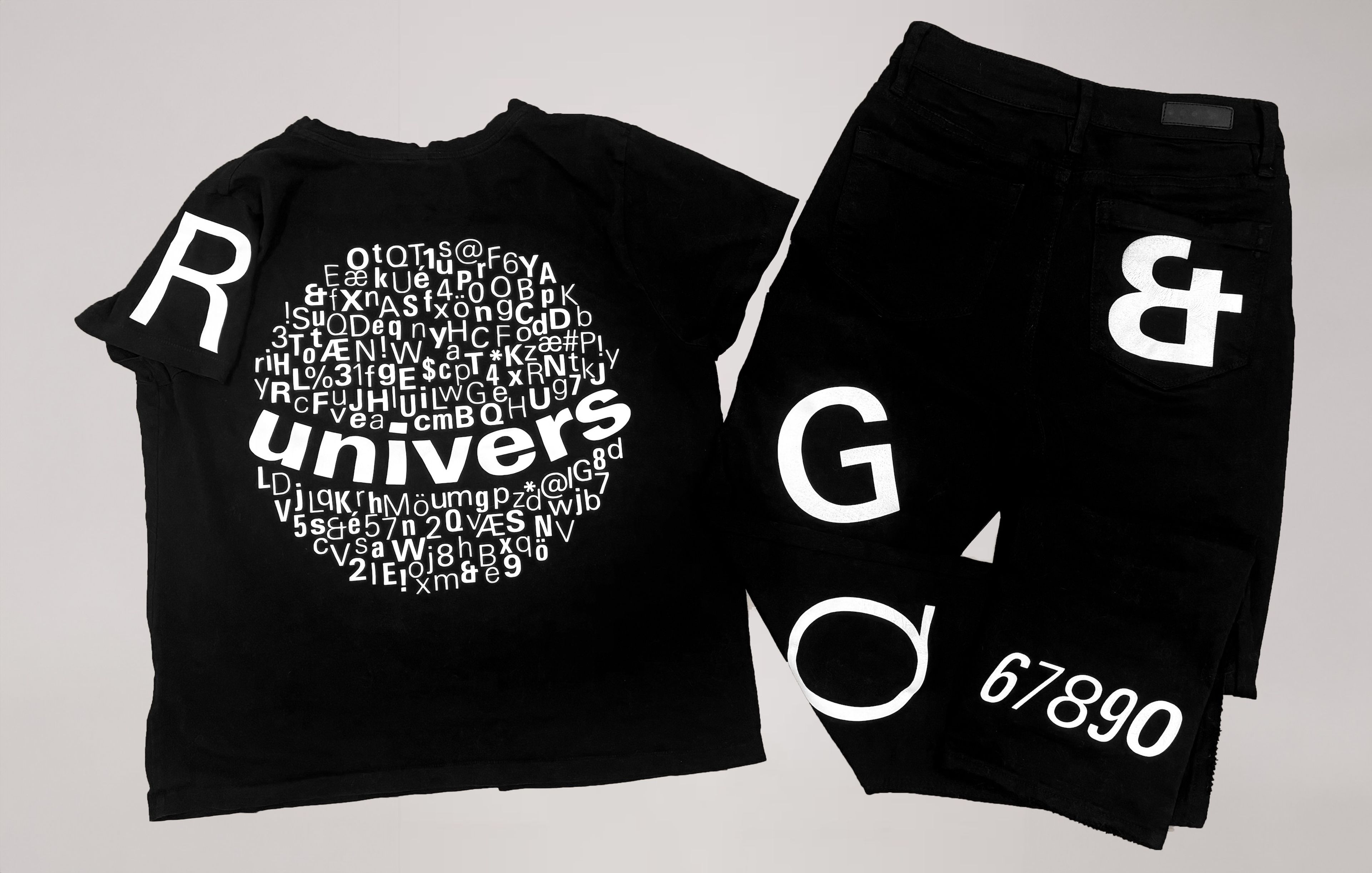 A set of black clothing items – a T-shirt and jeans – with bold, white, typographic designs. The T-shirt features the word “Univers” in large white letters surrounded by smaller letters and symbols, forming a circular design. The jeans display large white letters and numbers on the front and back pockets.