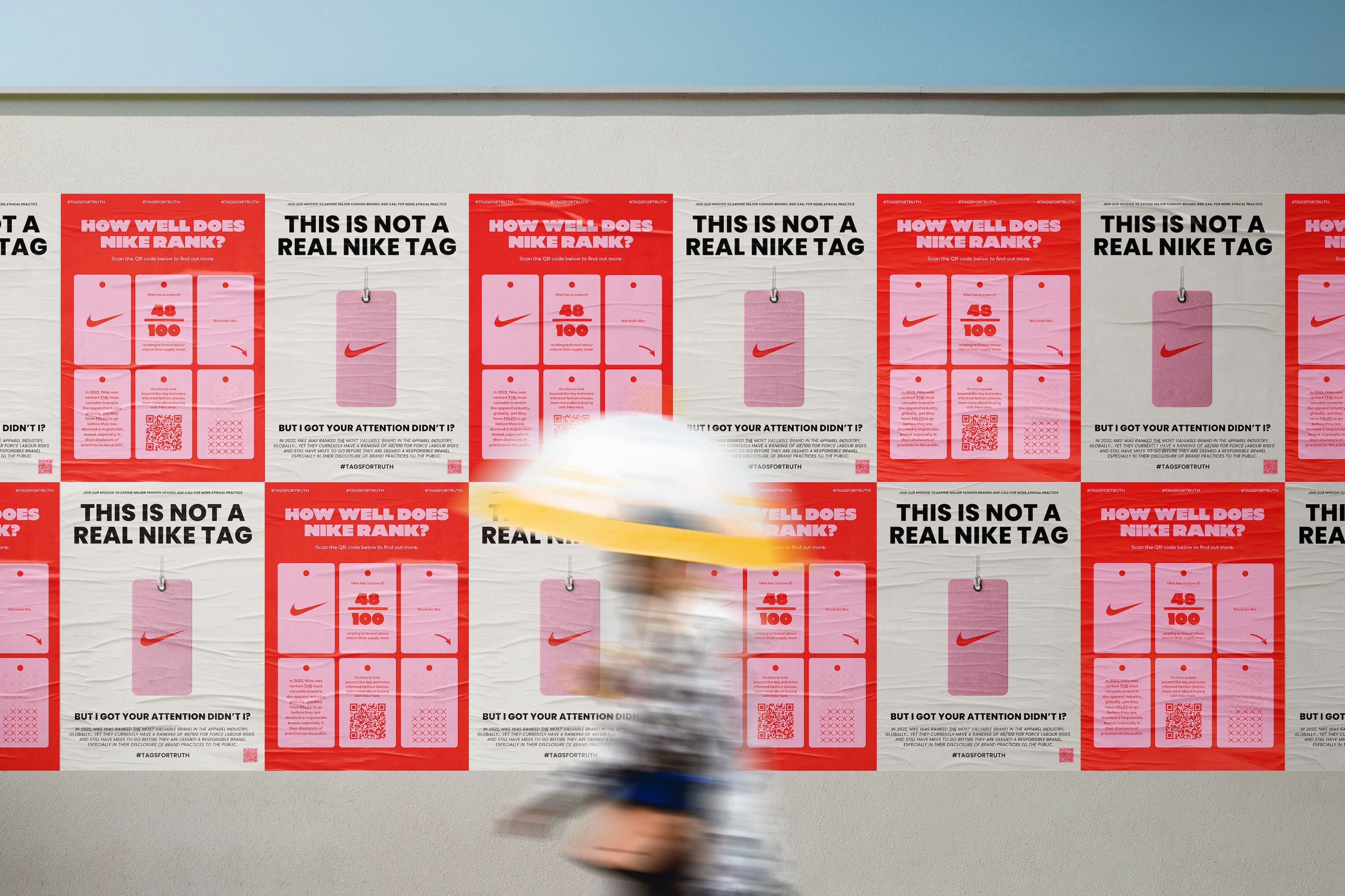 A series of red and pink posters lining a wall with the heading "THIS IS NOT A REAL NIKE TAG" in bold black text. Some posters read, "How well does Nike rank?" with a large Nike logo, QR code, and ratings to prompt viewer engagement.