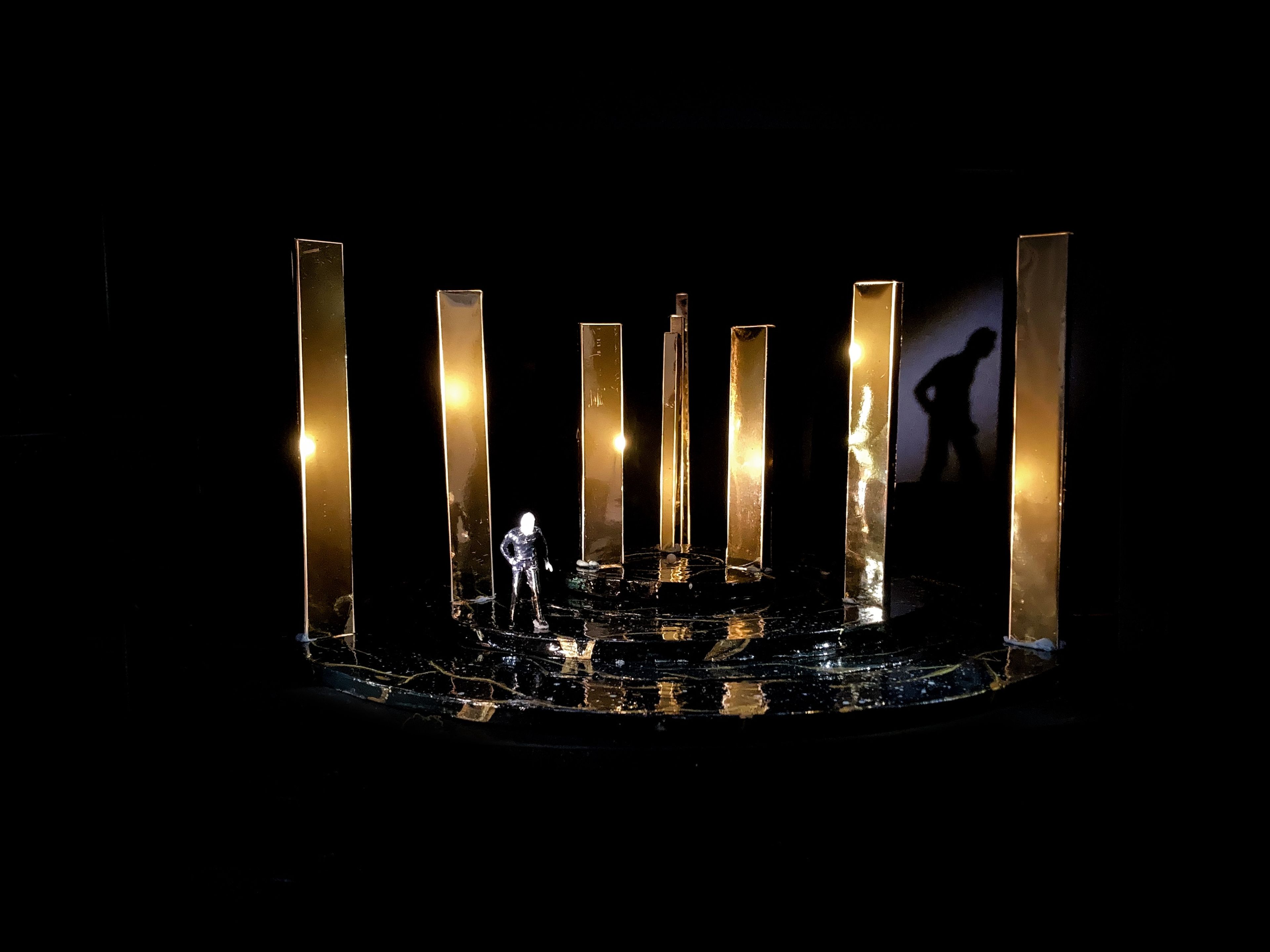 Stage model for Act 5, Scene 5, showing an arrangement of illuminated golden panels and a solitary figure casting a shadow.