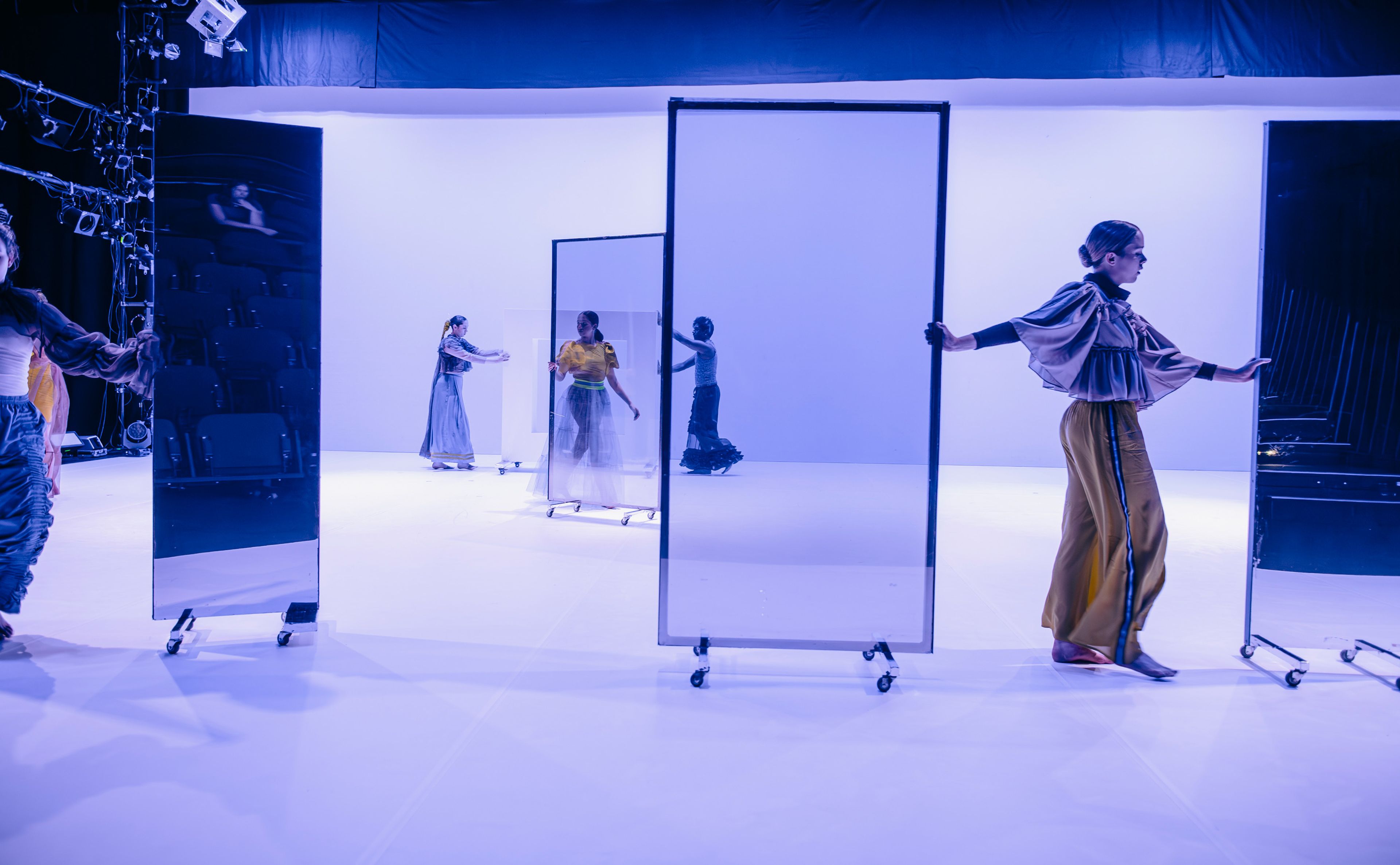 Dance production photograph of several dancers moving with large, framed panels in a minimalist, softly lit stage space.