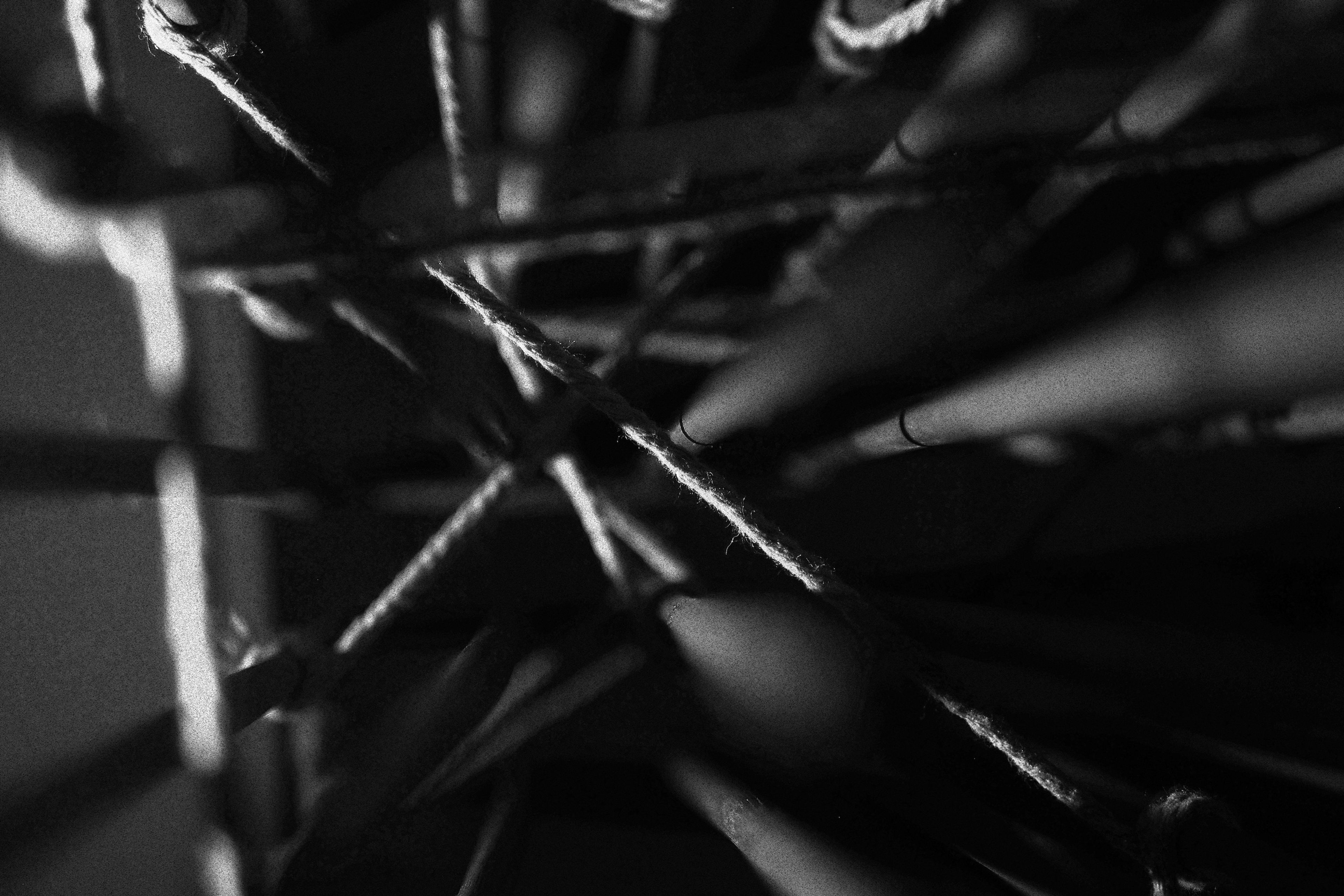 Black-and-white close-up of tangled ropes creating an abstract, web-like structure. Dark shadows and high contrast evoke a sense of mystery and complexity.