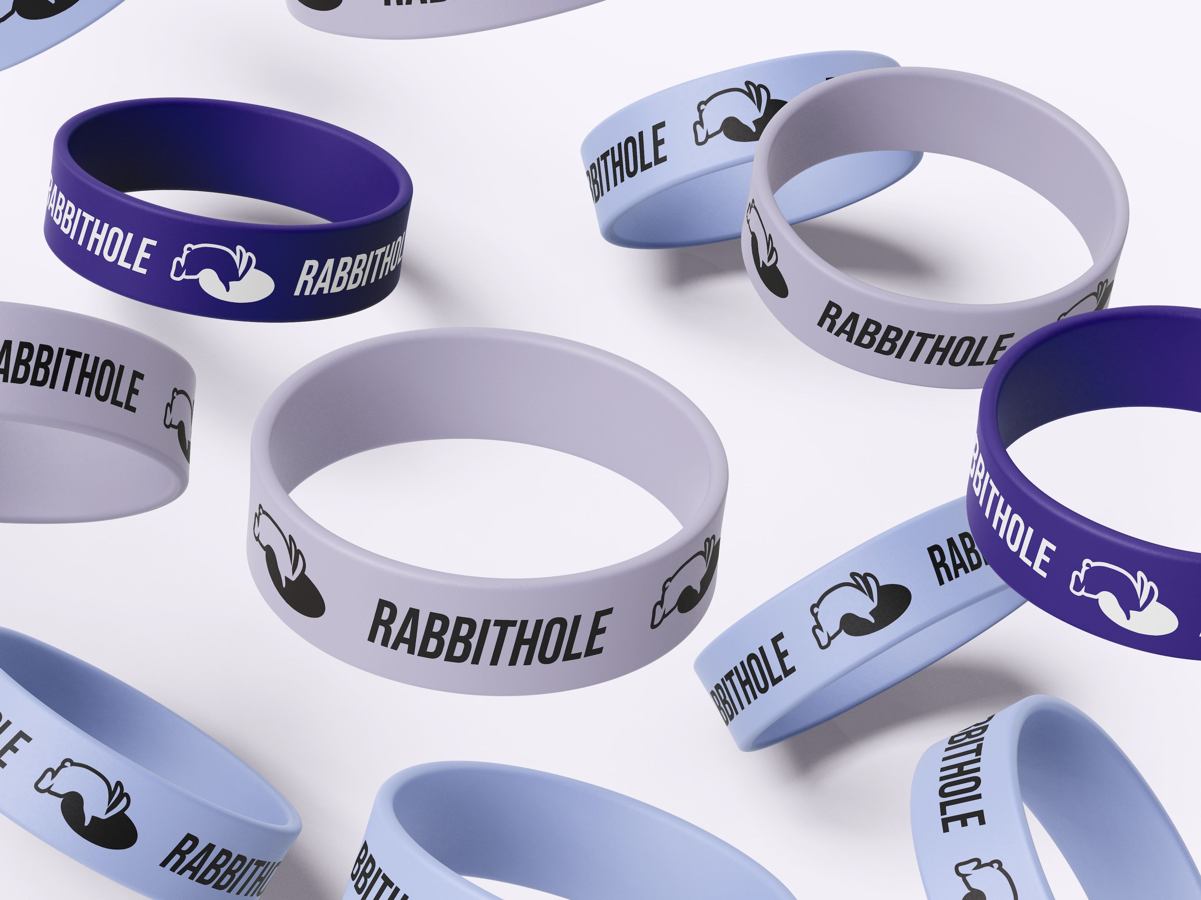 Collection of silicone wristbands in shades of purple and blue, branded with the 'Rabbithole Game Lounge' name and logo. Each band displays the text and logo in a repeating pattern, creating a playful, casual merchandise design.