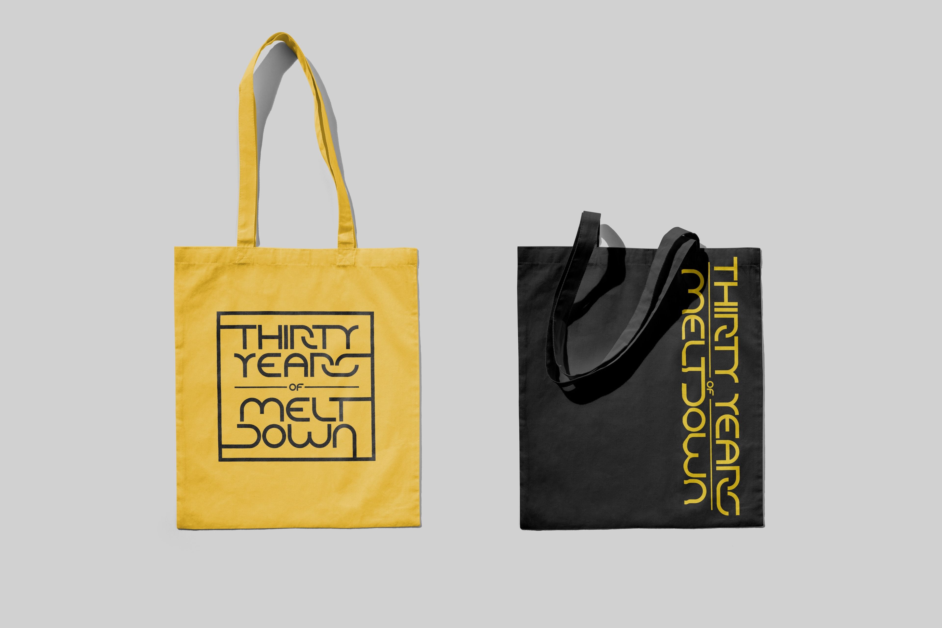 Two tote bags, one yellow with black text and the other black with yellow text, each reading “Thirty Years of Meltdown” in a bold, stylized font. The simple colour contrast and retro typography create a striking, memorable design.