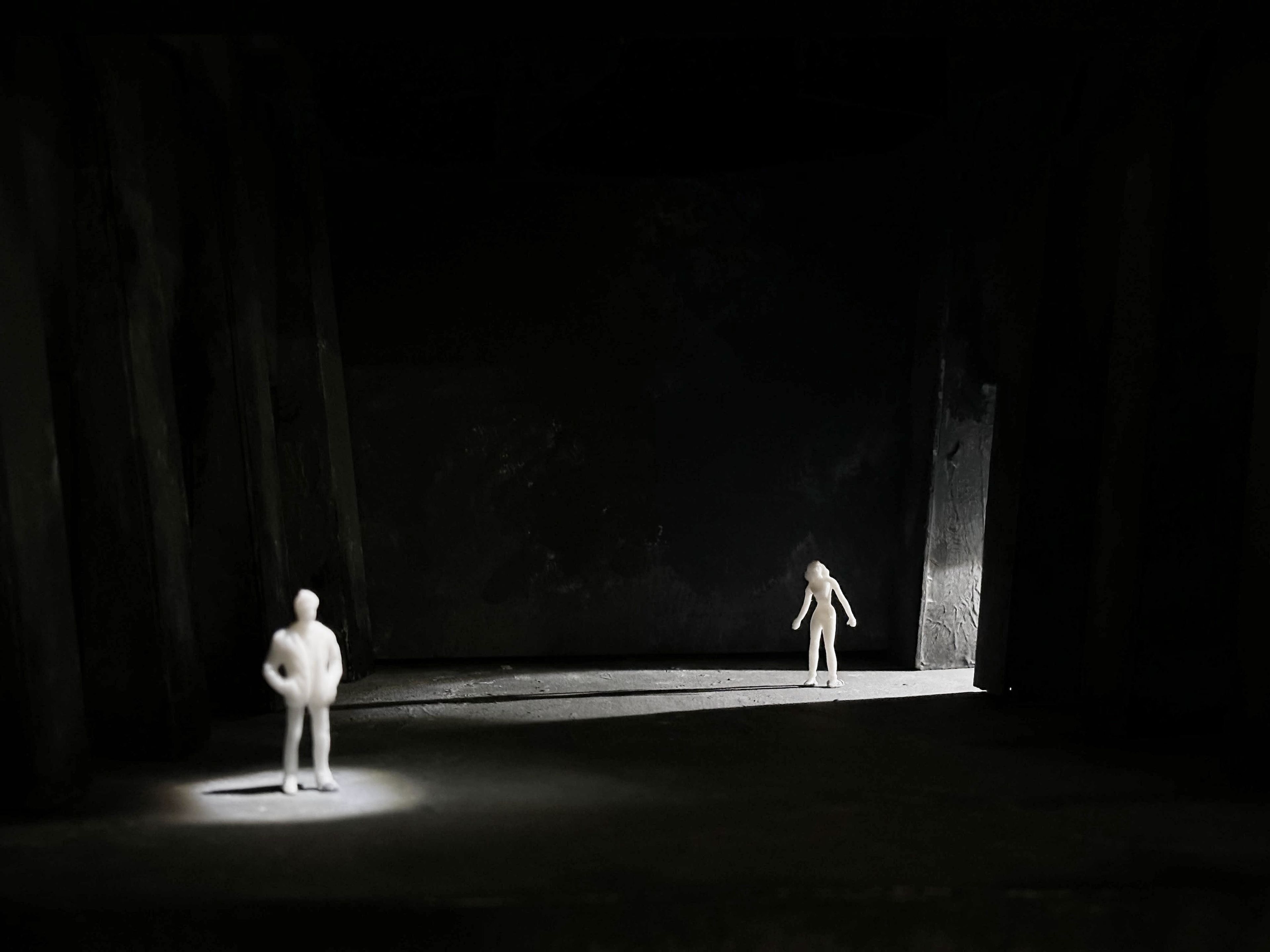 Dark stage model with two figures separated by spotlights, creating an atmospheric scene with shadows.