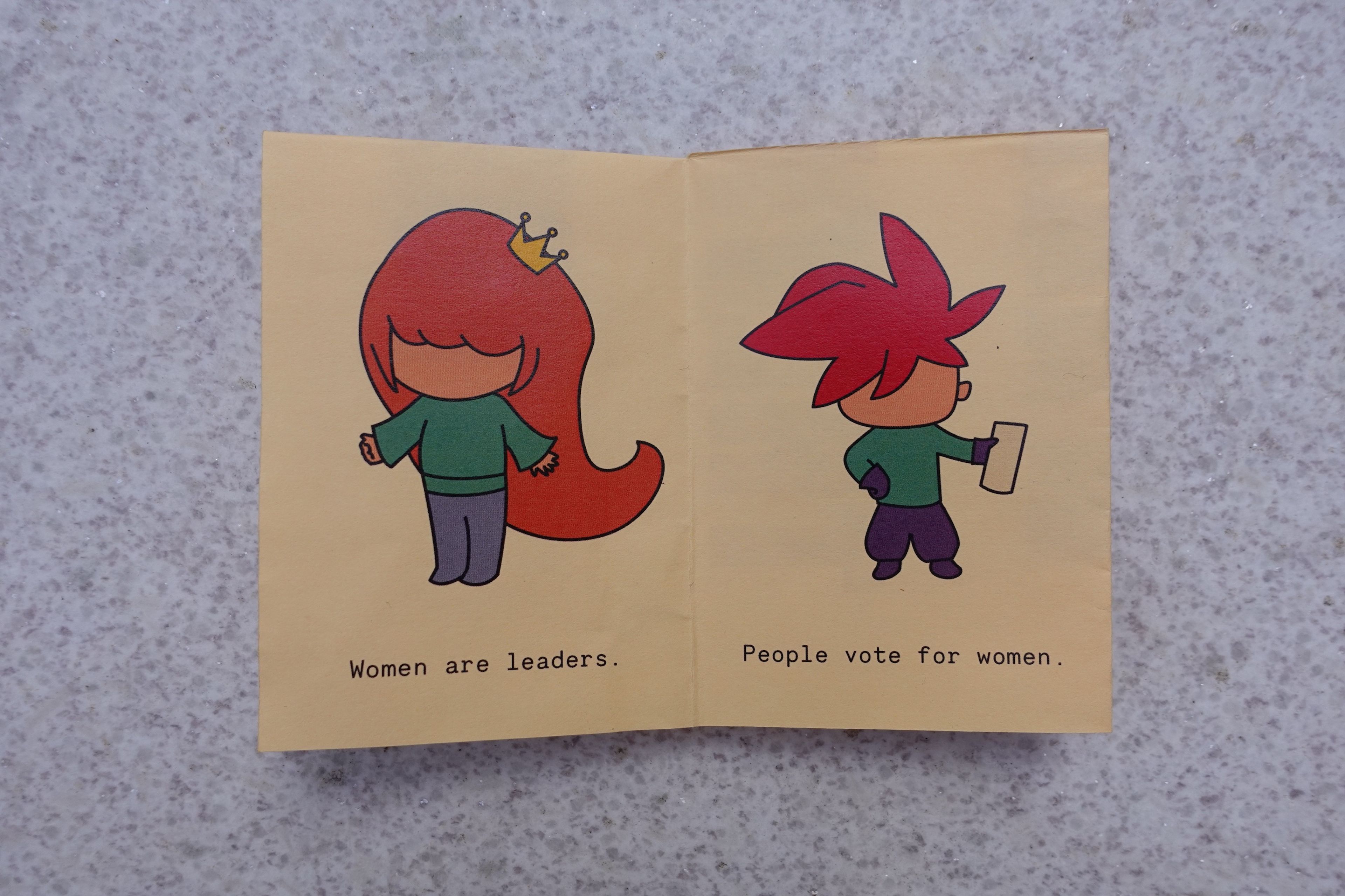 Two-page spread from the "Women's Rights" zine featuring minimalist cartoon characters. The character on the left, with long red hair and a crown, represents women as leaders, while the character on the right, with spiky red hair, holds a voting card. The text reads, "Women are leaders. People vote for women."