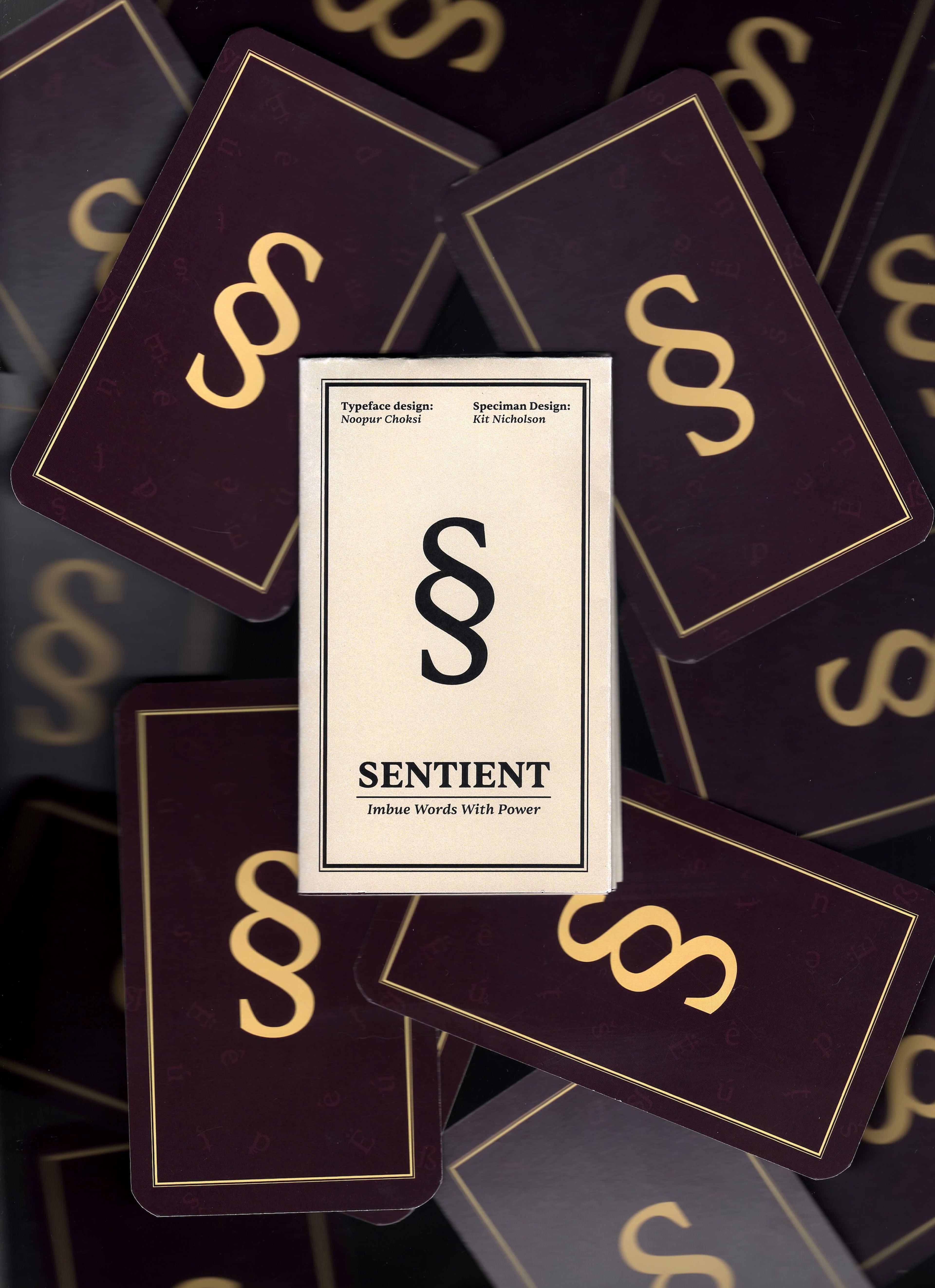 Type specimen for the "Sentient" typeface. The card features a sophisticated "§" symbol in the center, with the tagline "Imbue Words With Power" below, set against a backdrop of richly coloured specimen cards, highlighting the typeface's elegance and authority.