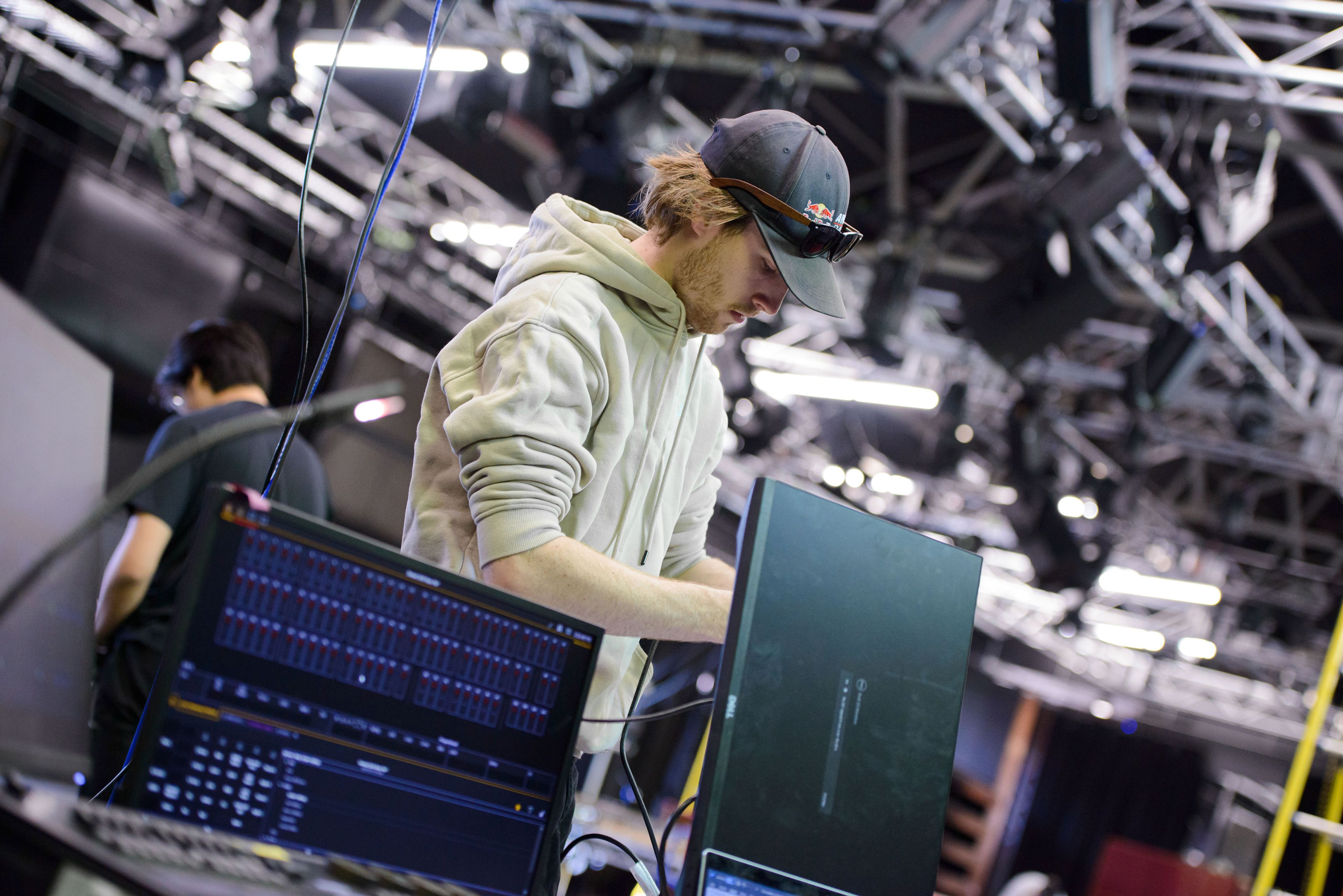 A person in a light hoodie and cap works to connect monitor to lighting console