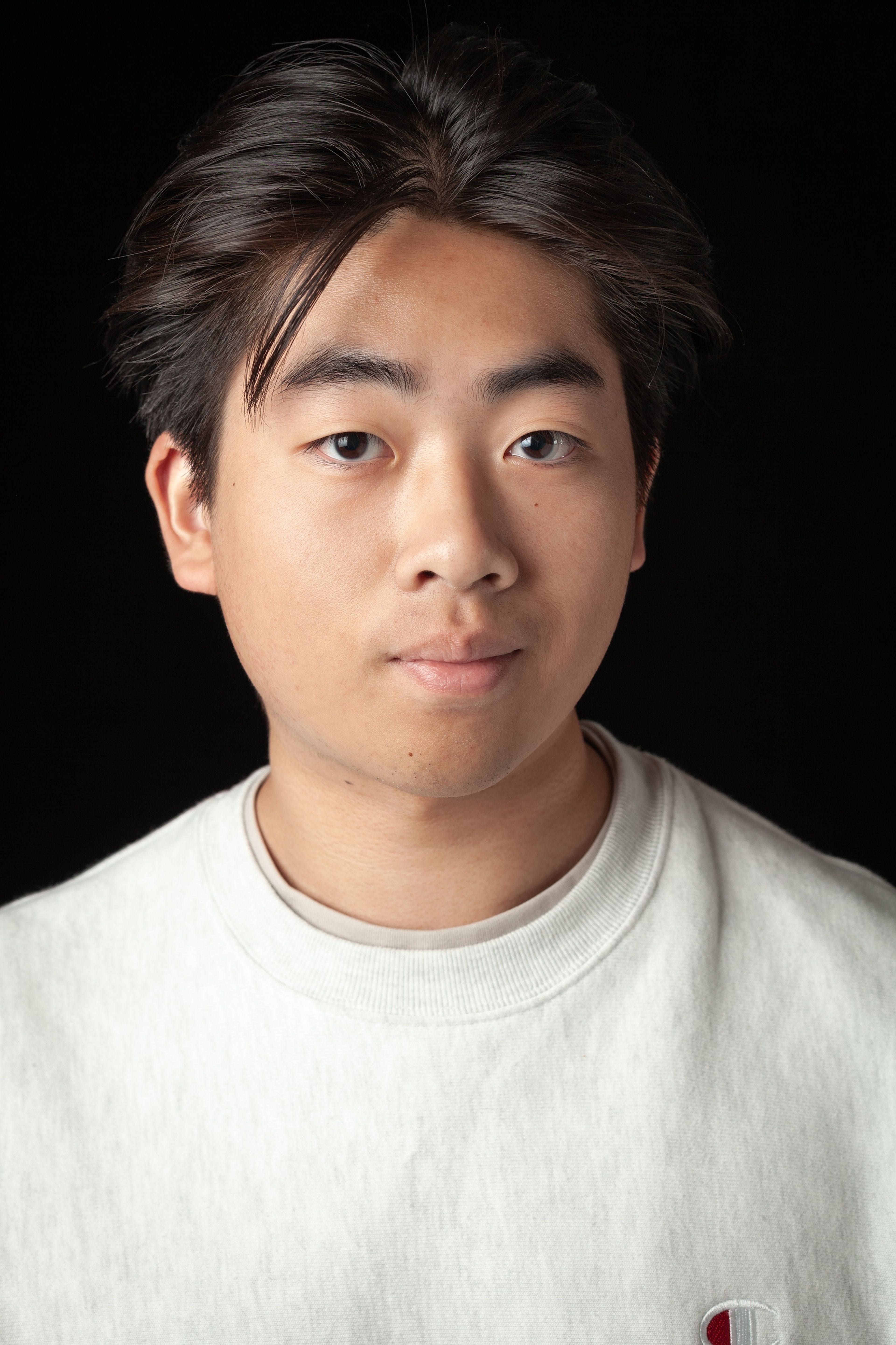 Headshot of a young man with short dark hair, wearing a light grey sweatshirt, against a black background.