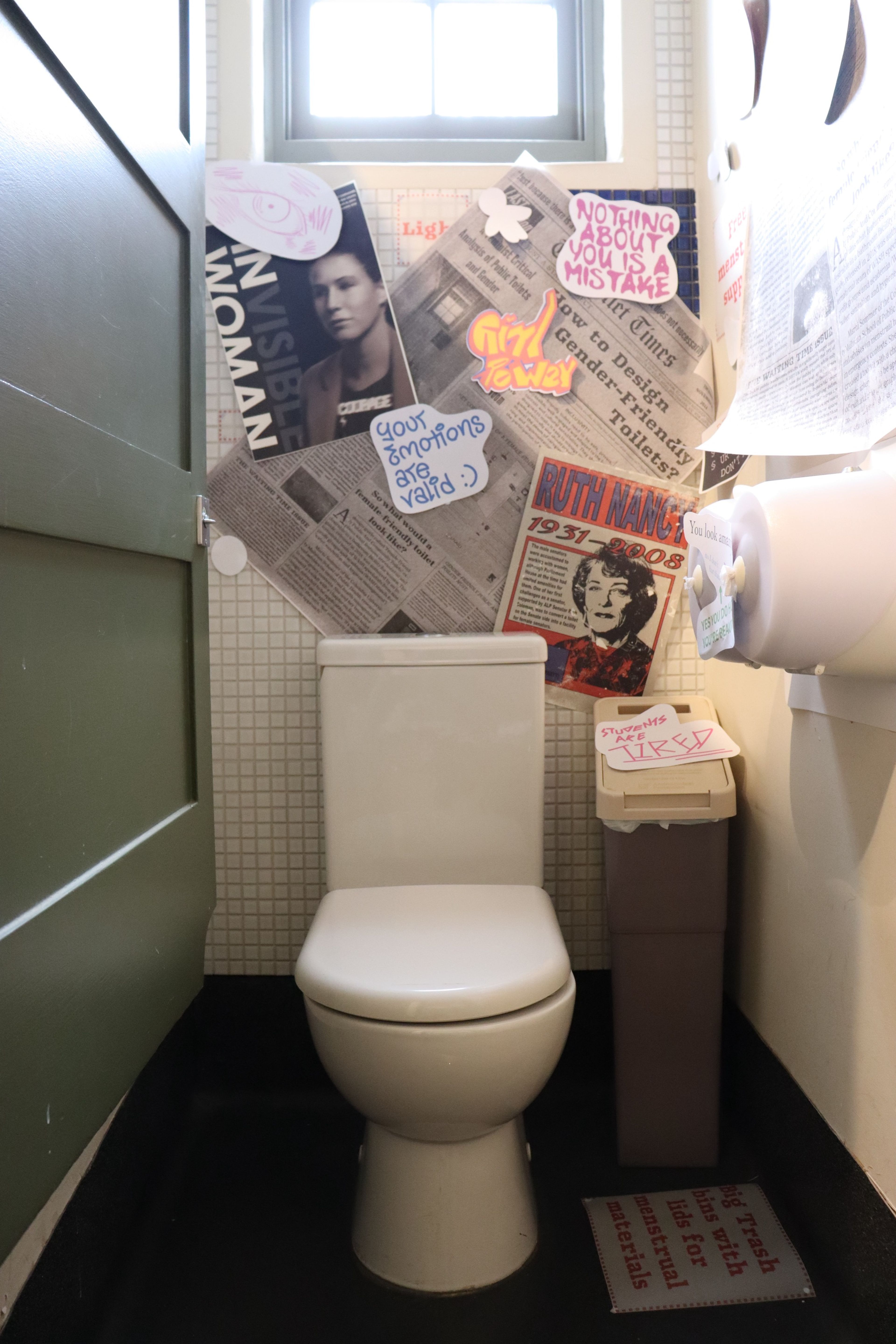 Restroom interior featuring a wall collage which combines vintage newspaper clippings, fashion magazine images, and handwritten notes in an artistic arrangement.