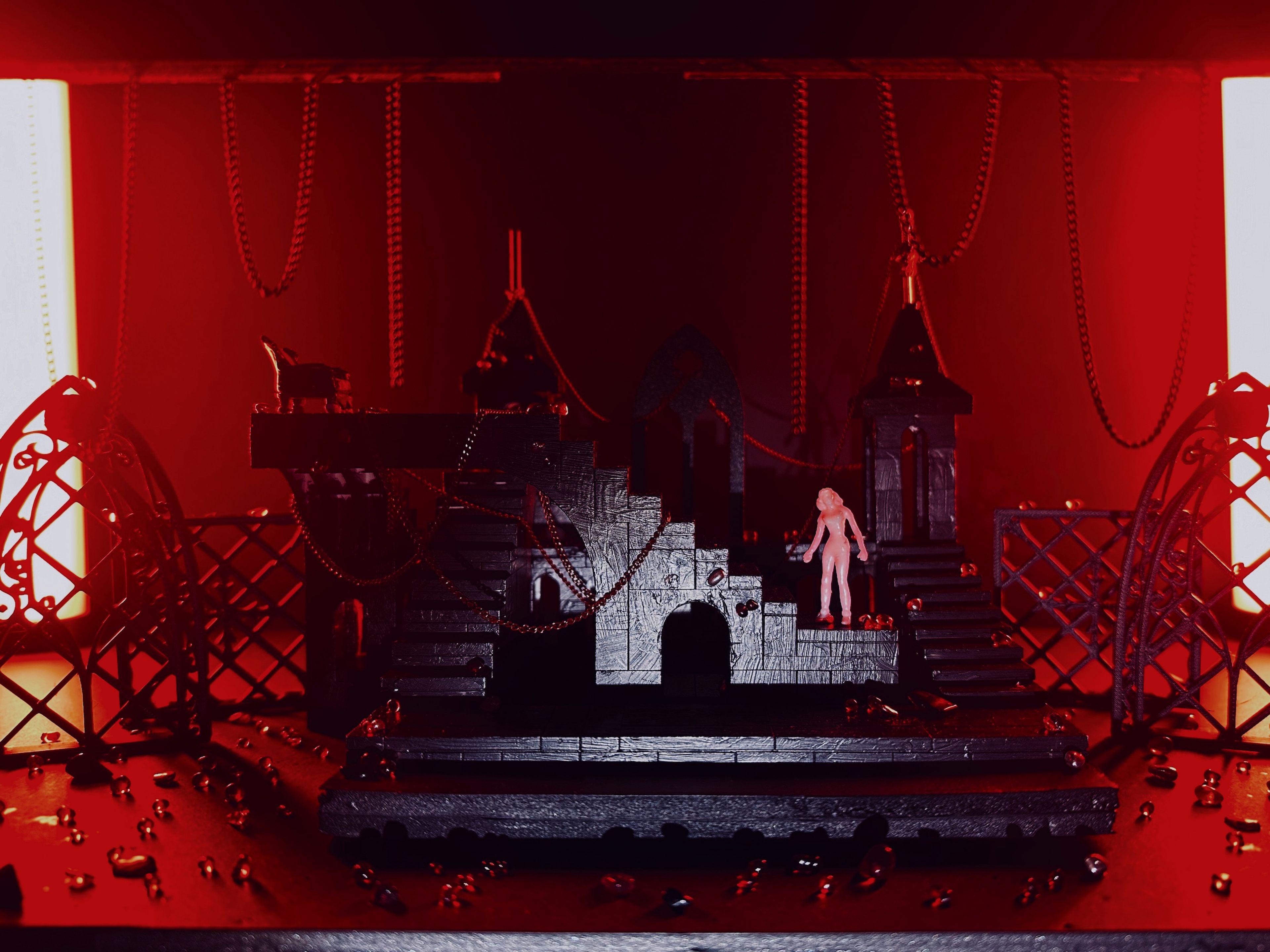 Gothic-style set model with chains and red beads, dramatically lit in red, with a single white figure on the staircase.