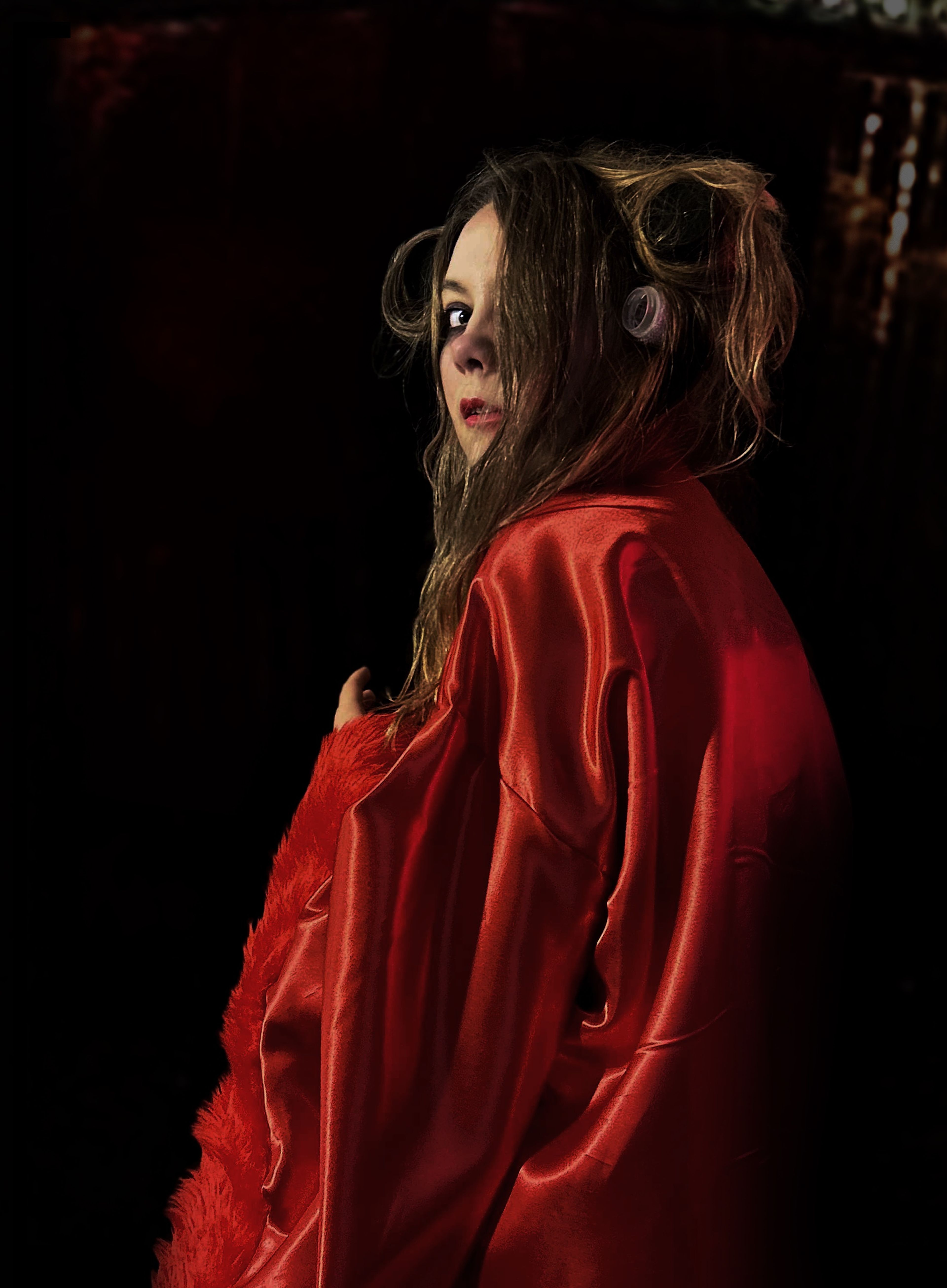 Portrait of a woman with long, dishevelled hair, wearing a red satin robe, looking over her shoulder with a serious expression.