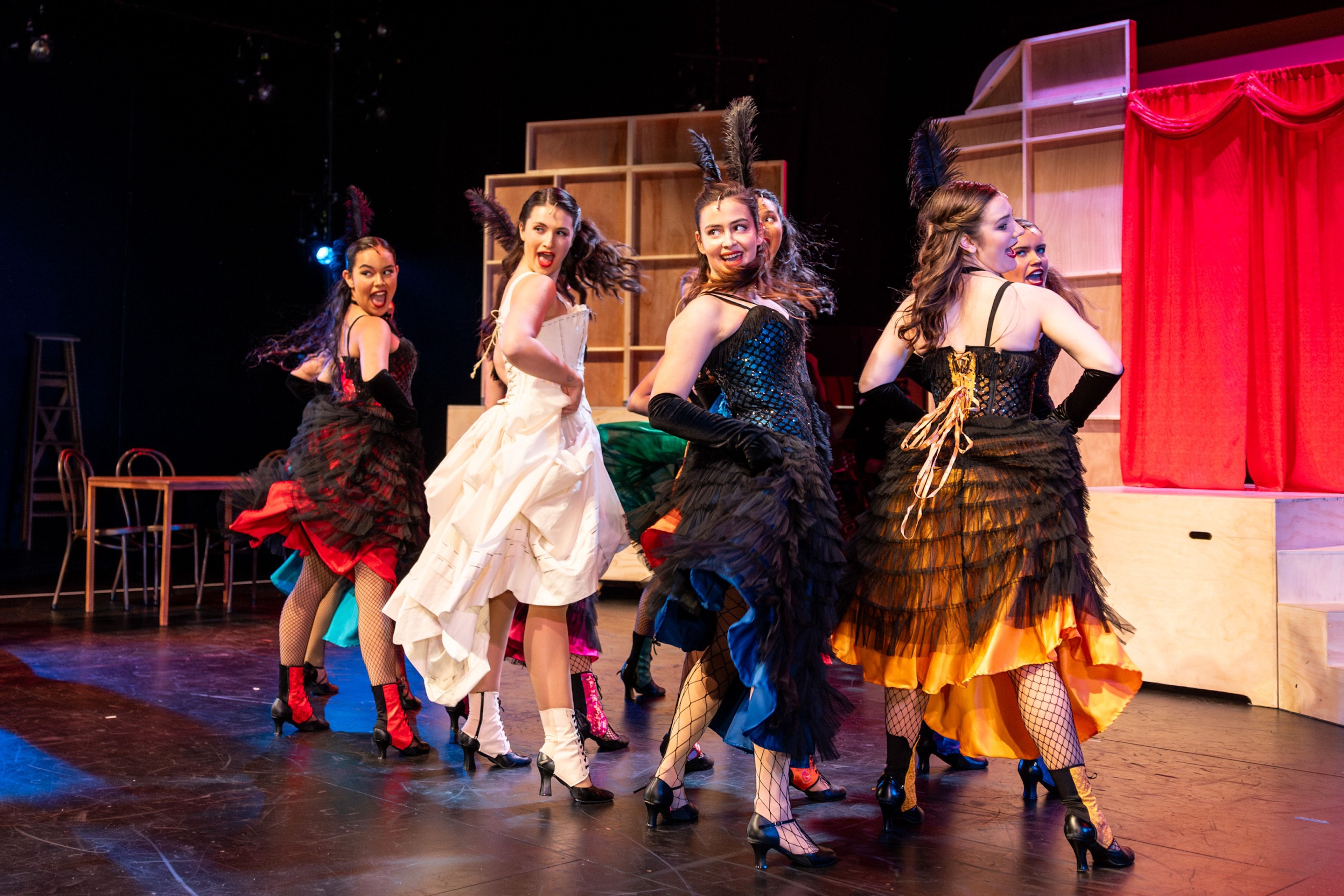 Theatre production photograph showing a group of dancers in black fringed and layered skirts.