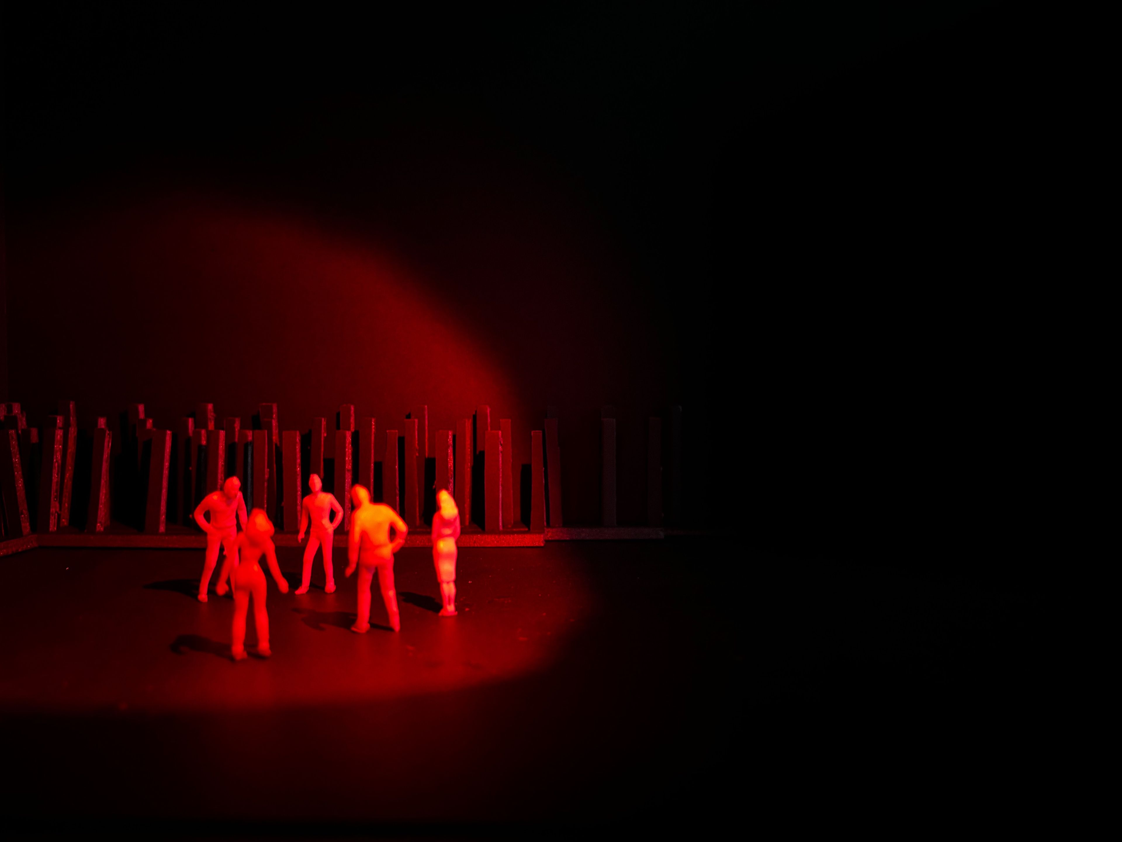 Stage model featuring five figures in red light, with dark vertical structures in the background.