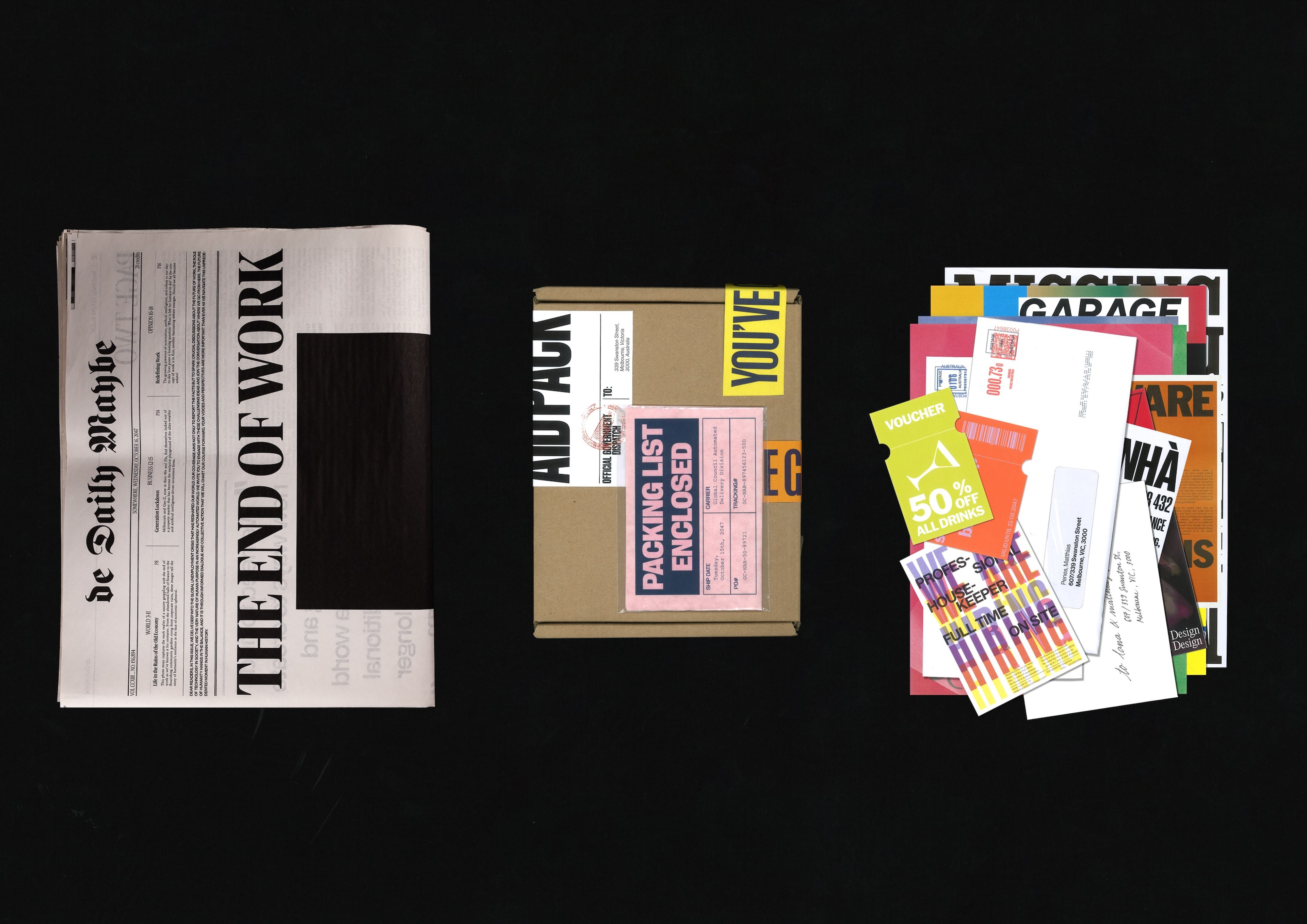 Various printed materials including a newspaper titled "The Daily Maybe" with a bold "THE END OF WORK" headline, a cardboard box labeled with stickers like "Packing List Enclosed," and a colorful spread of promotional cards, vouchers, and envelopes laid out against a black background.