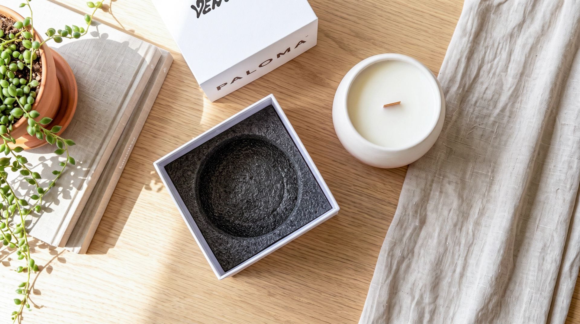 A top-down view of an unboxed white ceramic candle sitting next to its open white packaging box, which reveals a protective black EPE foam insert.