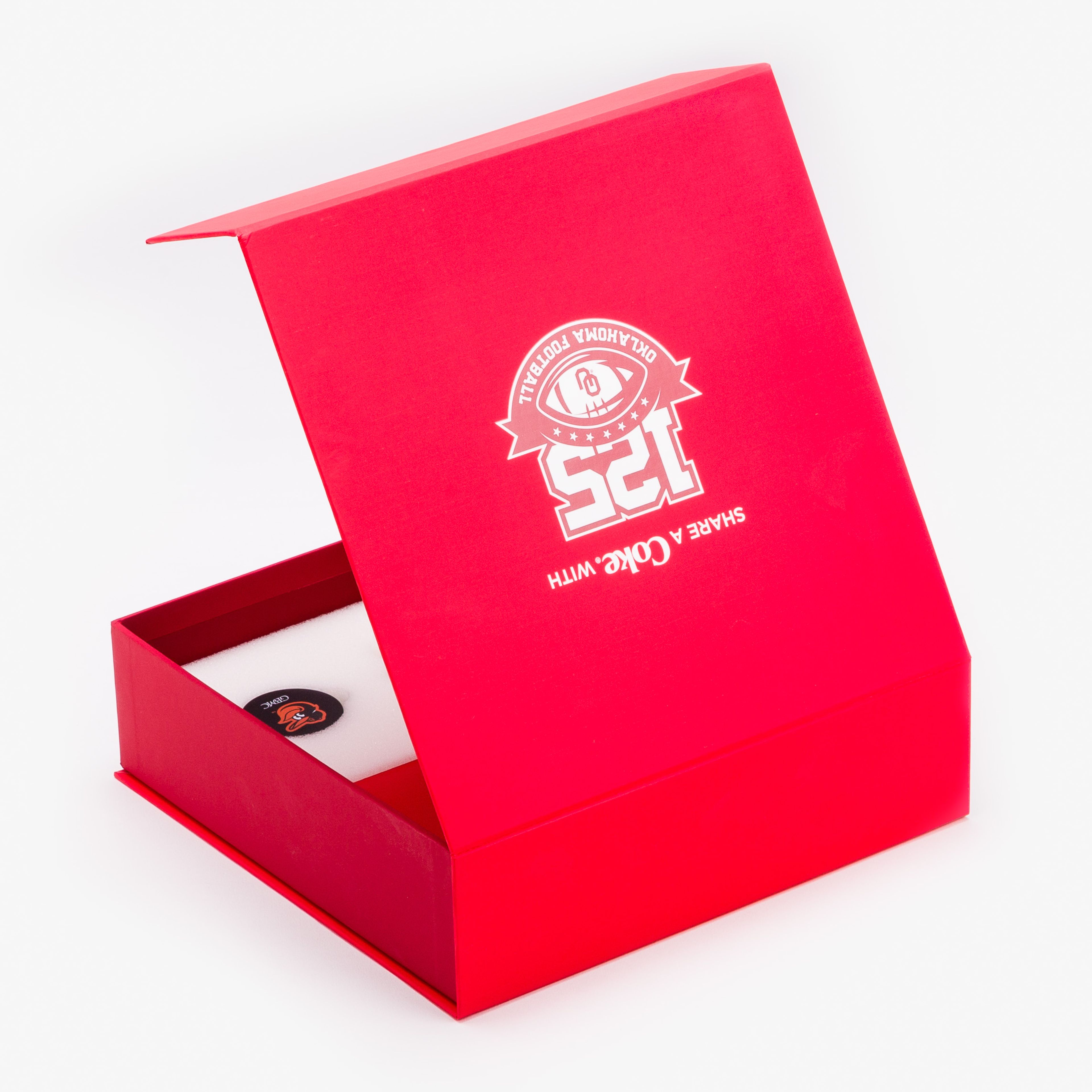 Slightly open red Coca-Cola gift box showing the Oklahoma Football 125th anniversary logo on the lid.