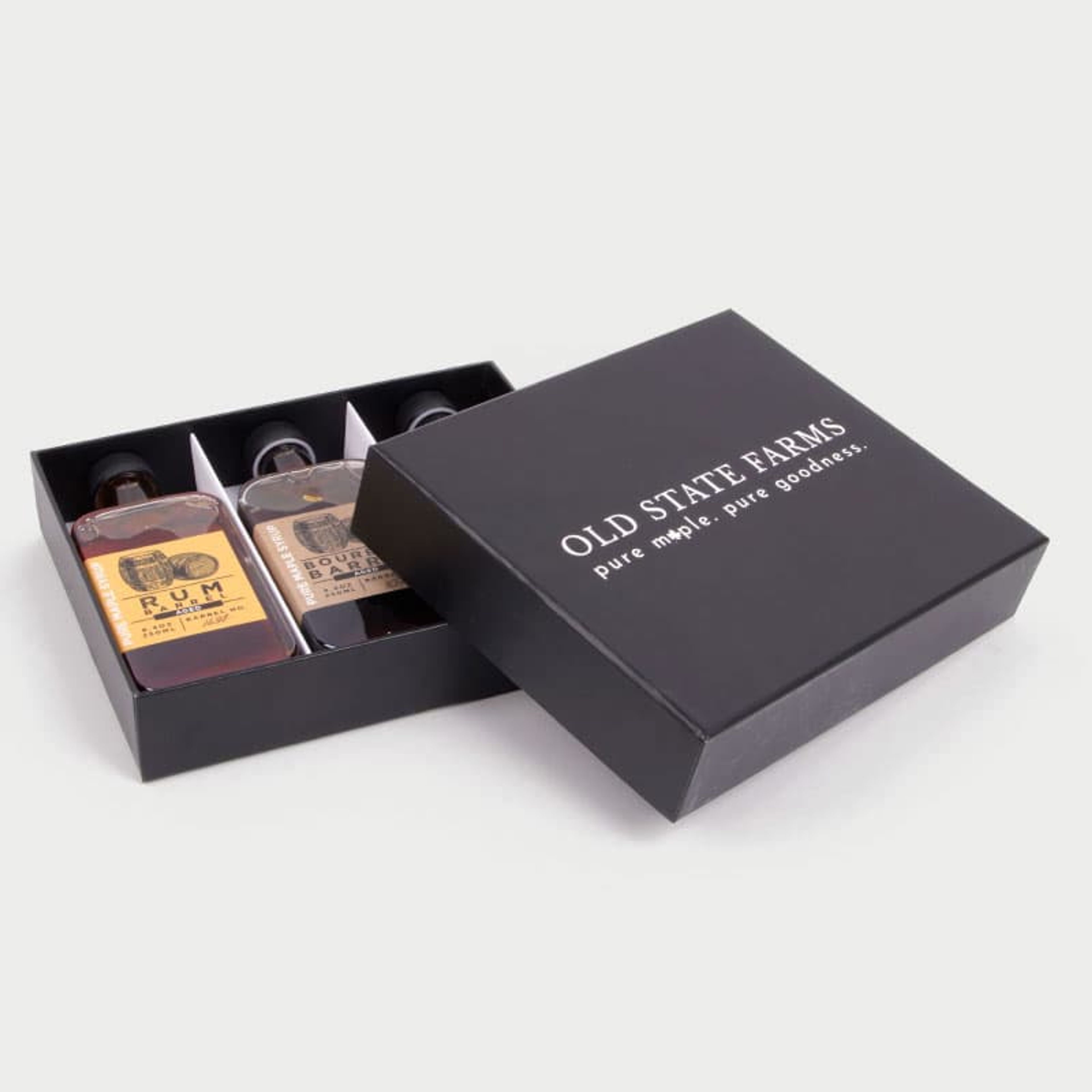 Angled view of an open Old State Farms black rigid box revealing three bottles of barrel-aged maple syrup inside.