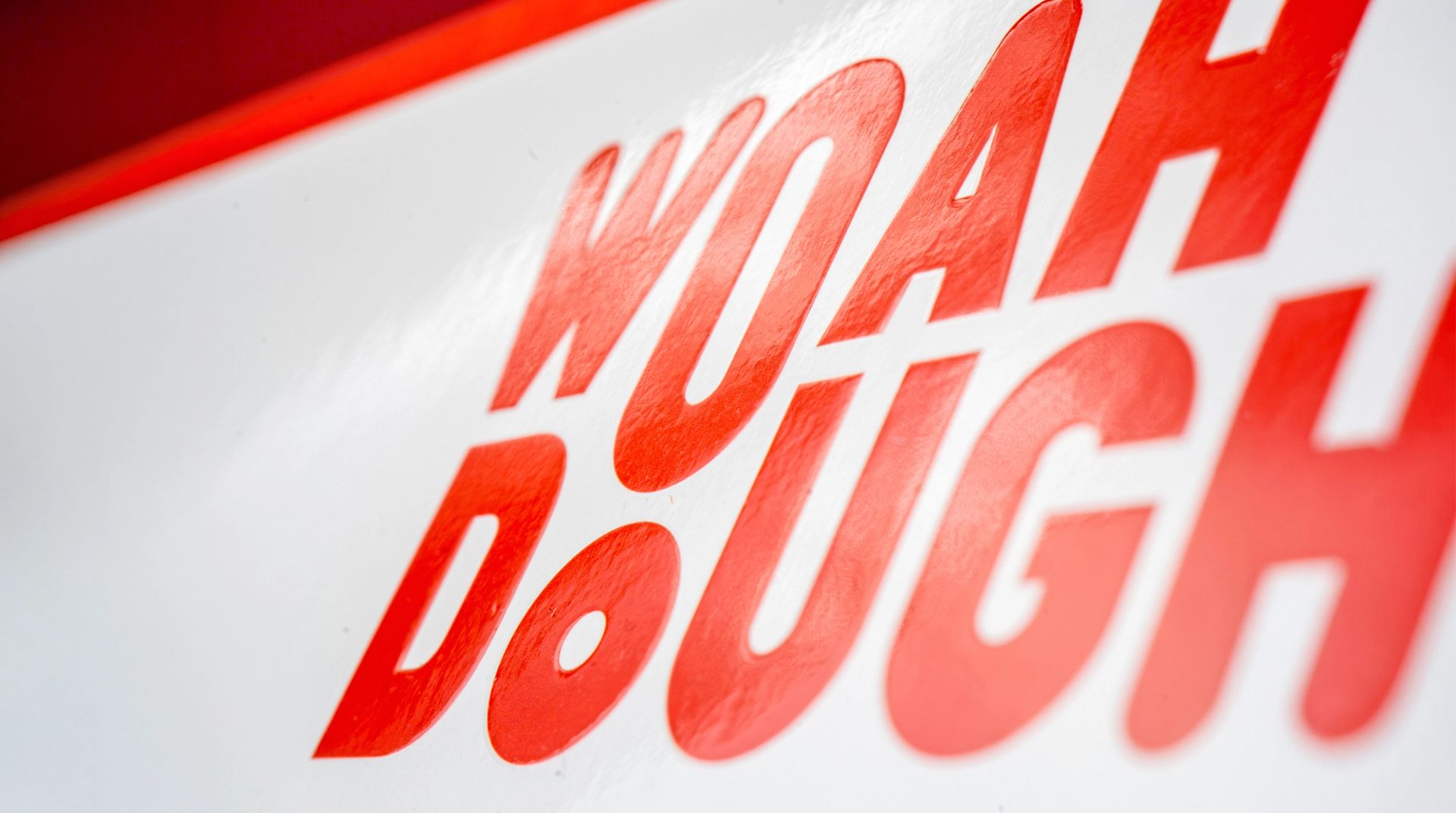 Close-up of the bright red Woah Dough logo featuring a glossy, raised texture on a white packaging surface.