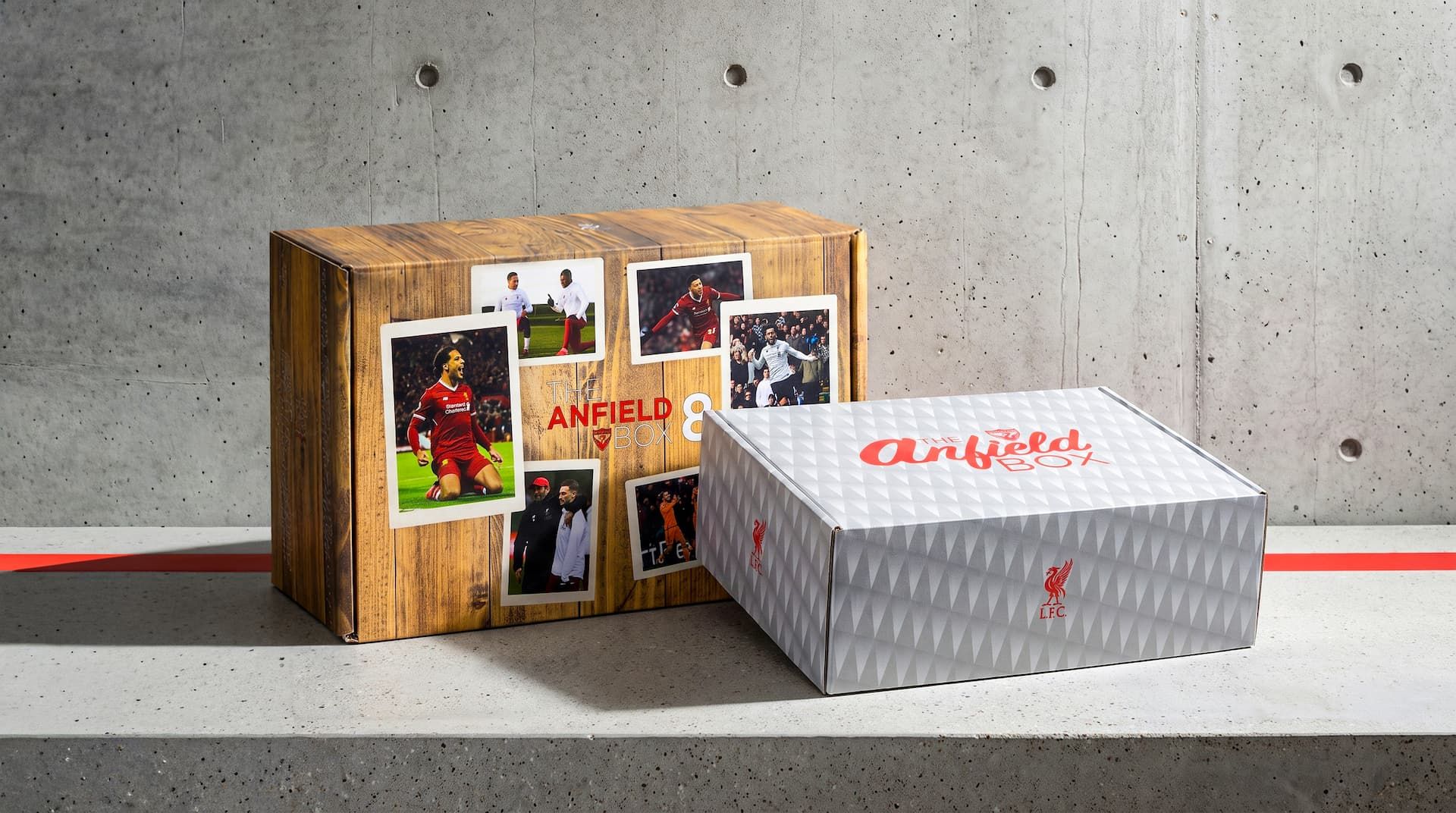 Two Liverpool FC subscription boxes on a concrete ledge, showcasing custom wood-grain and modern geometric exterior prints.