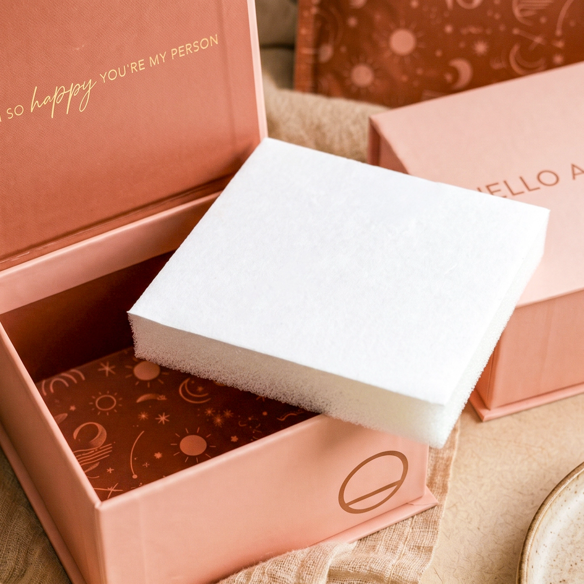A close-up of an open light pink jewelry box with a thick white flocked PU foam padding insert resting at an angle across its opening.