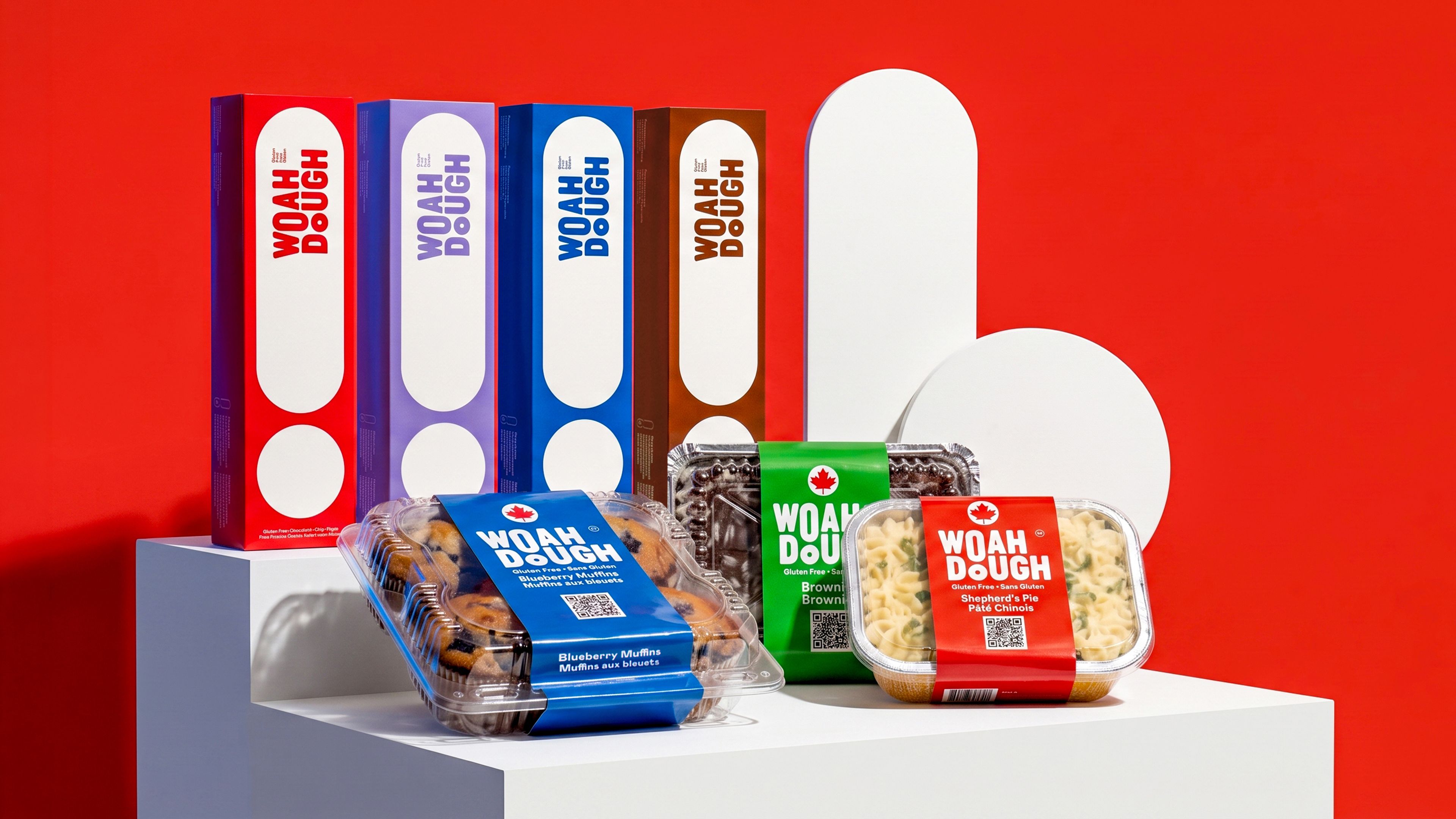 Colorful Woah Dough packaging including tall boxes and clear containers with blue, green, and red sleeves on white blocks.