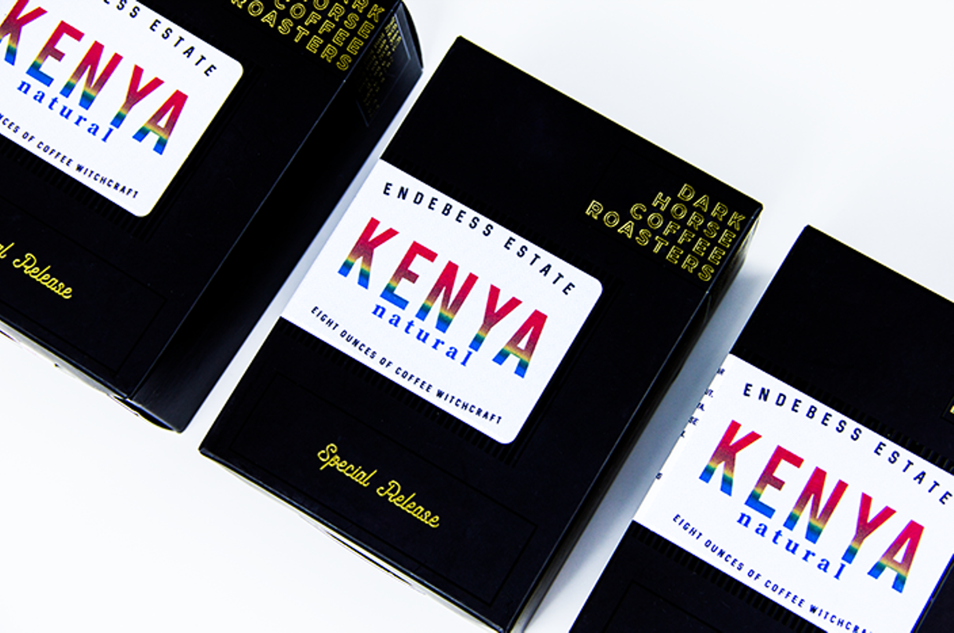 Three black Dark Horse Coffee boxes for Endebess Estate Kenya Natural with rainbow foil labels on a white surface.