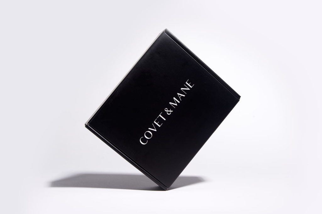A closed black Covet & Mane box with clean white typography balanced on one corner against a white background.