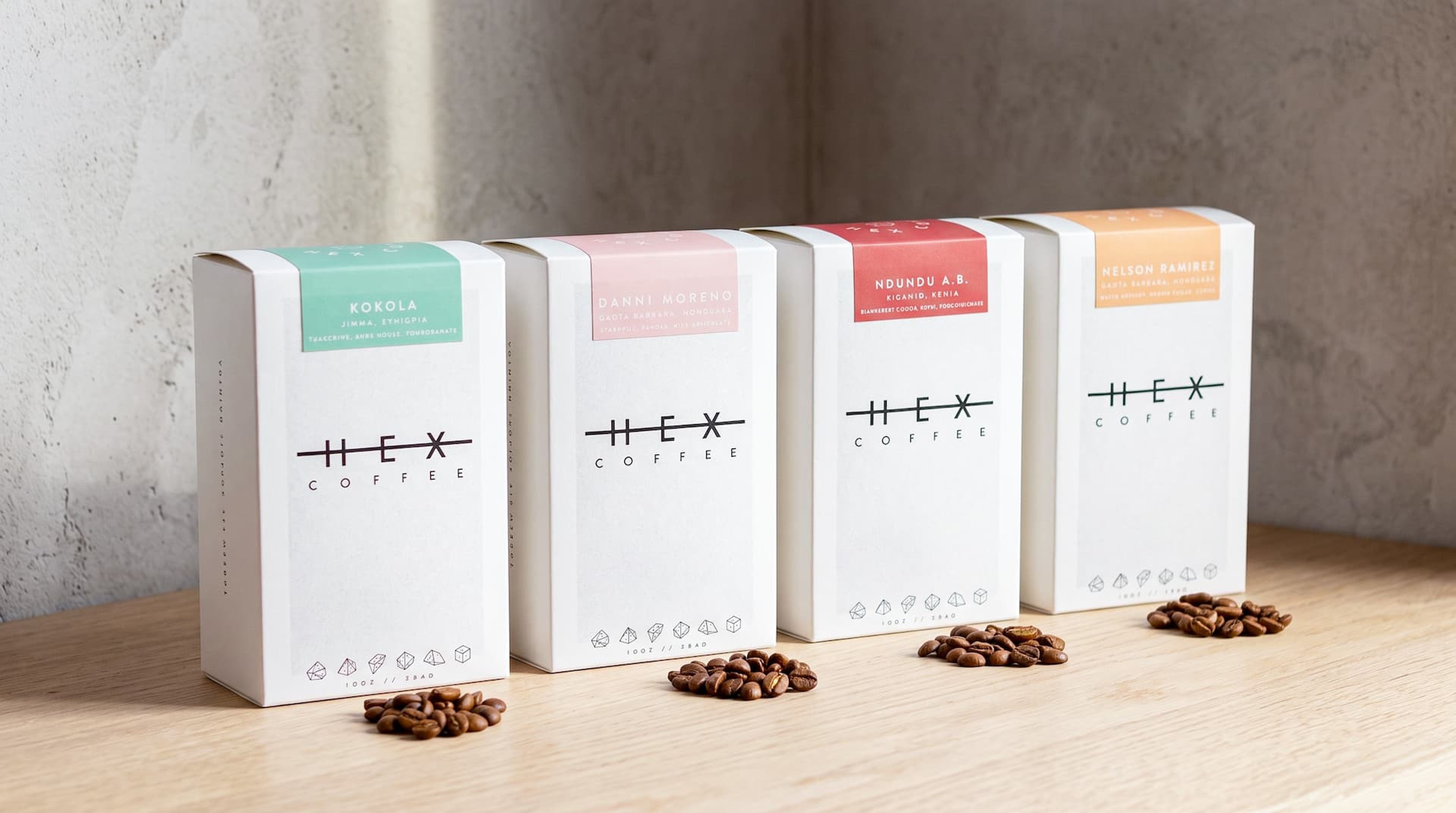 Four standing Hex Coffee boxes featuring pastel labels in green, pink, red, and orange, with coffee beans piled in front.