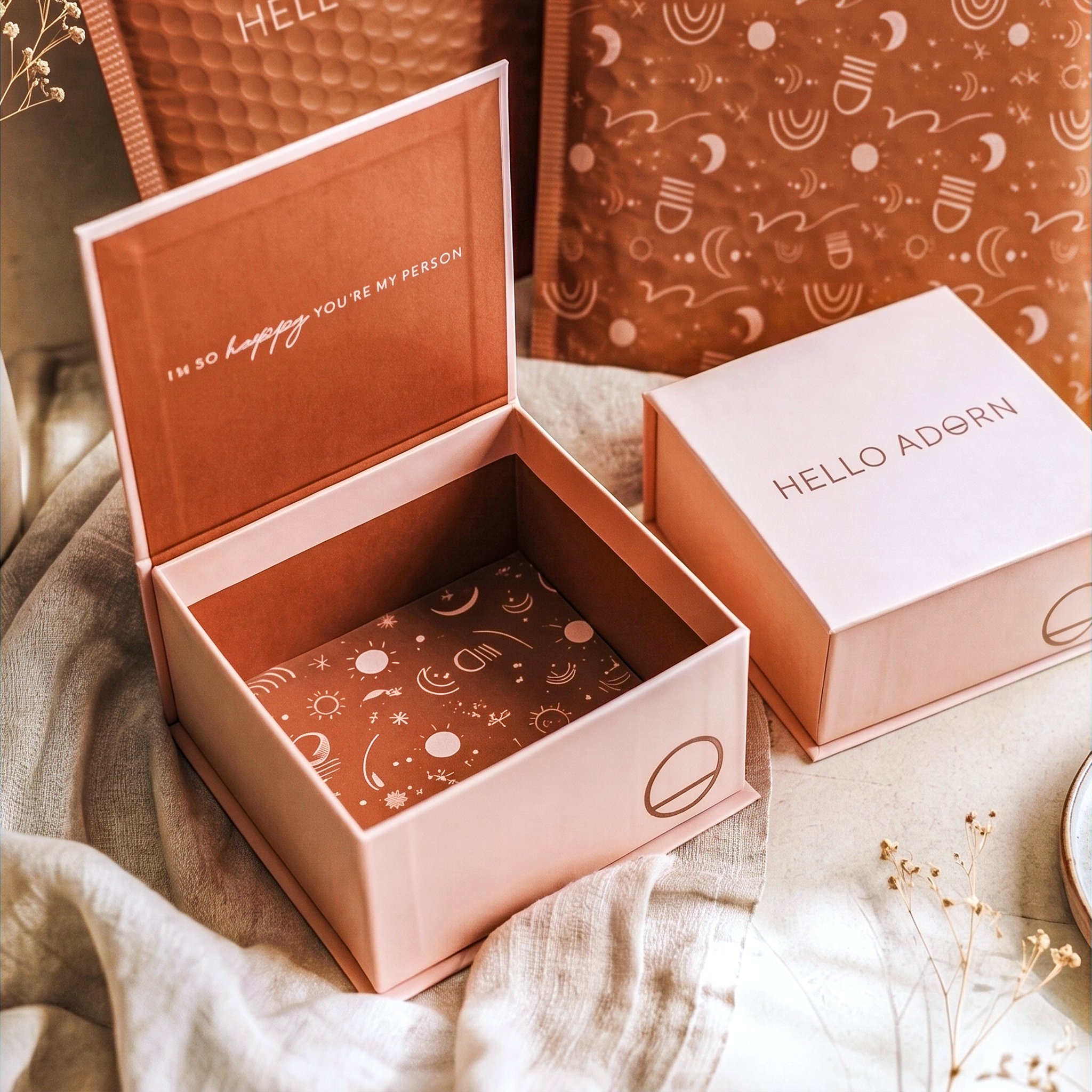 Two pink Hello Adorn jewelry boxes on beige fabric; one open with a rust interior reading "I'M SO happy YOU'RE MY PERSON."