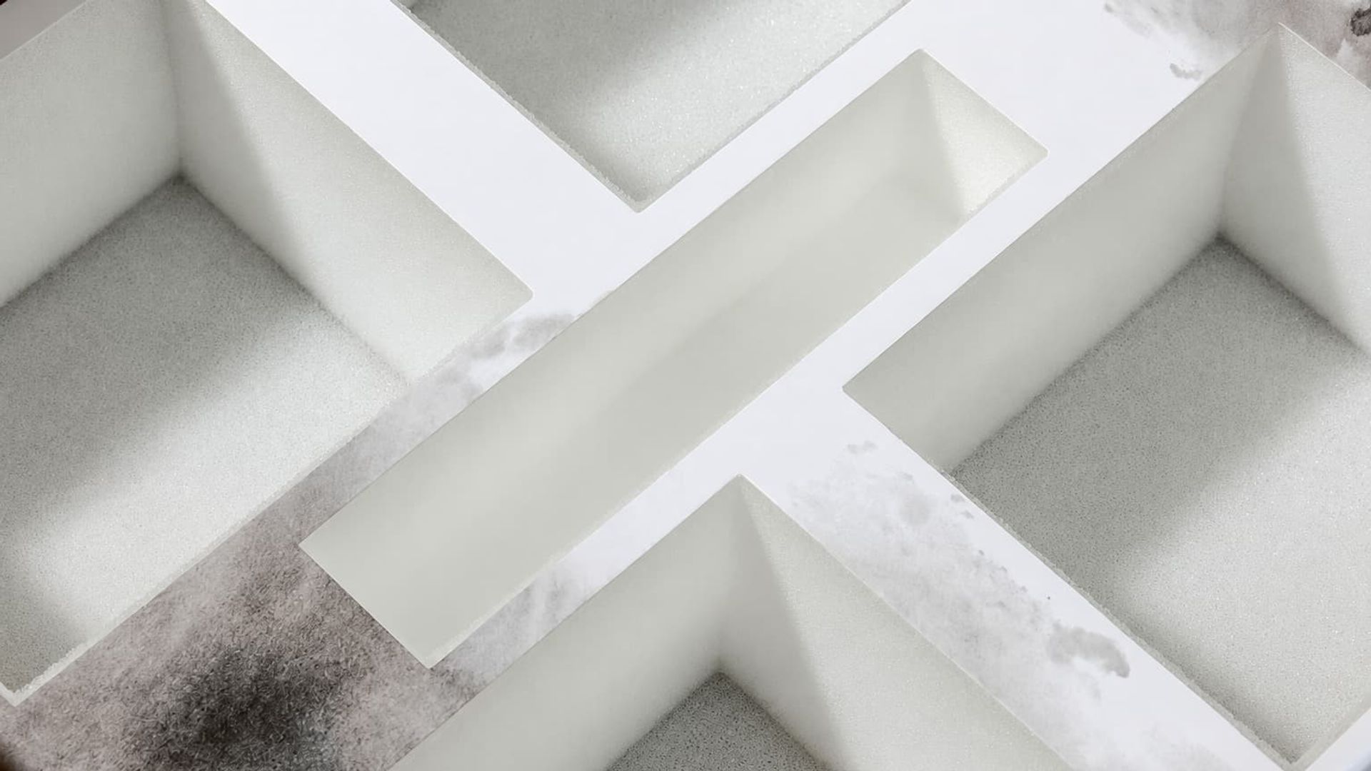Close-up of an empty white foam insert inside a box with cross-shaped dividers to securely hold four candles.