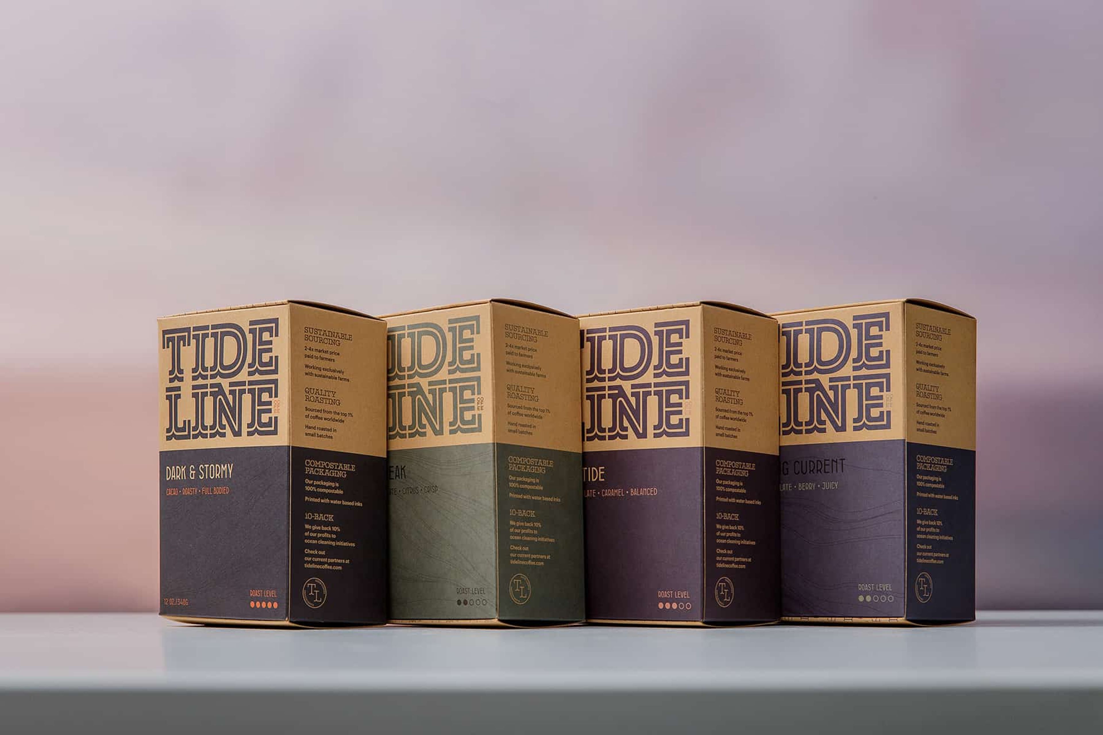 Four Tideline specialty coffee boxes lined up on a white surface against a soft sunset sky.