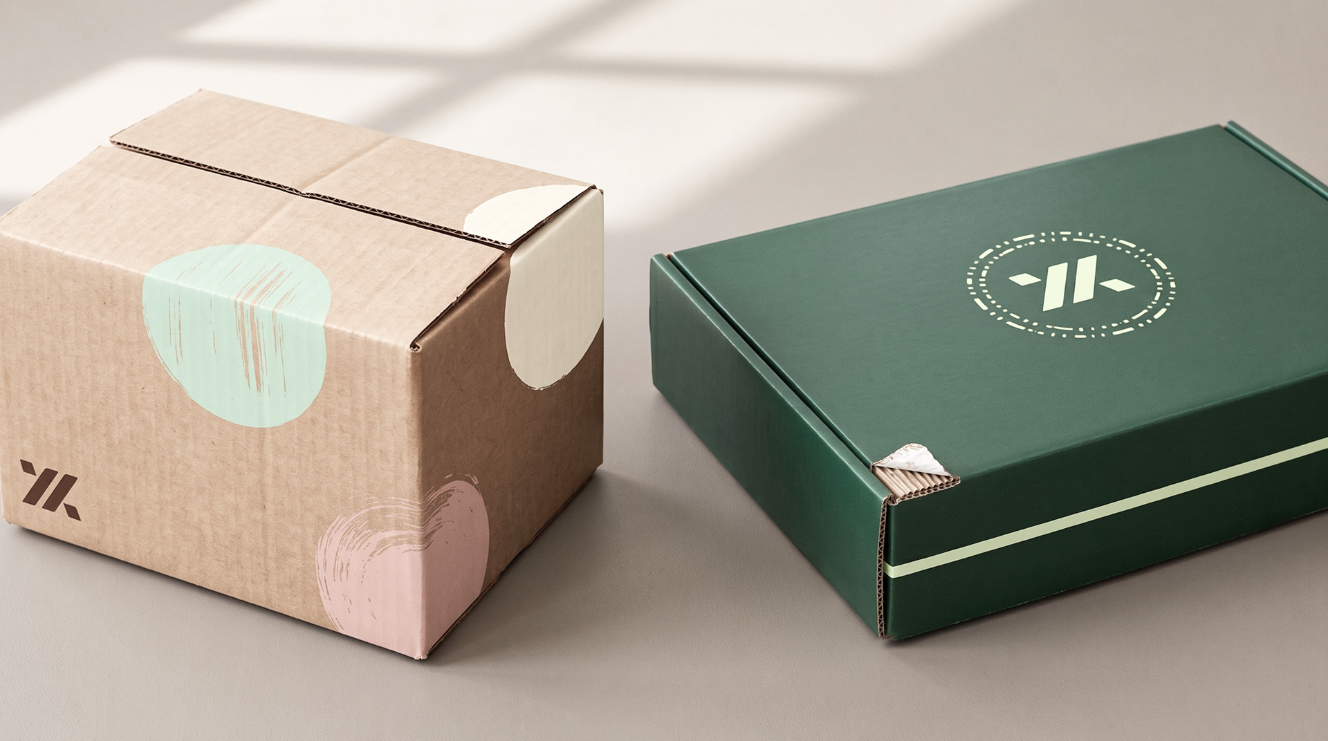 Kraft shipping box printed in pastel shapes beside a dark green mailer box with a smooth, even finish.
