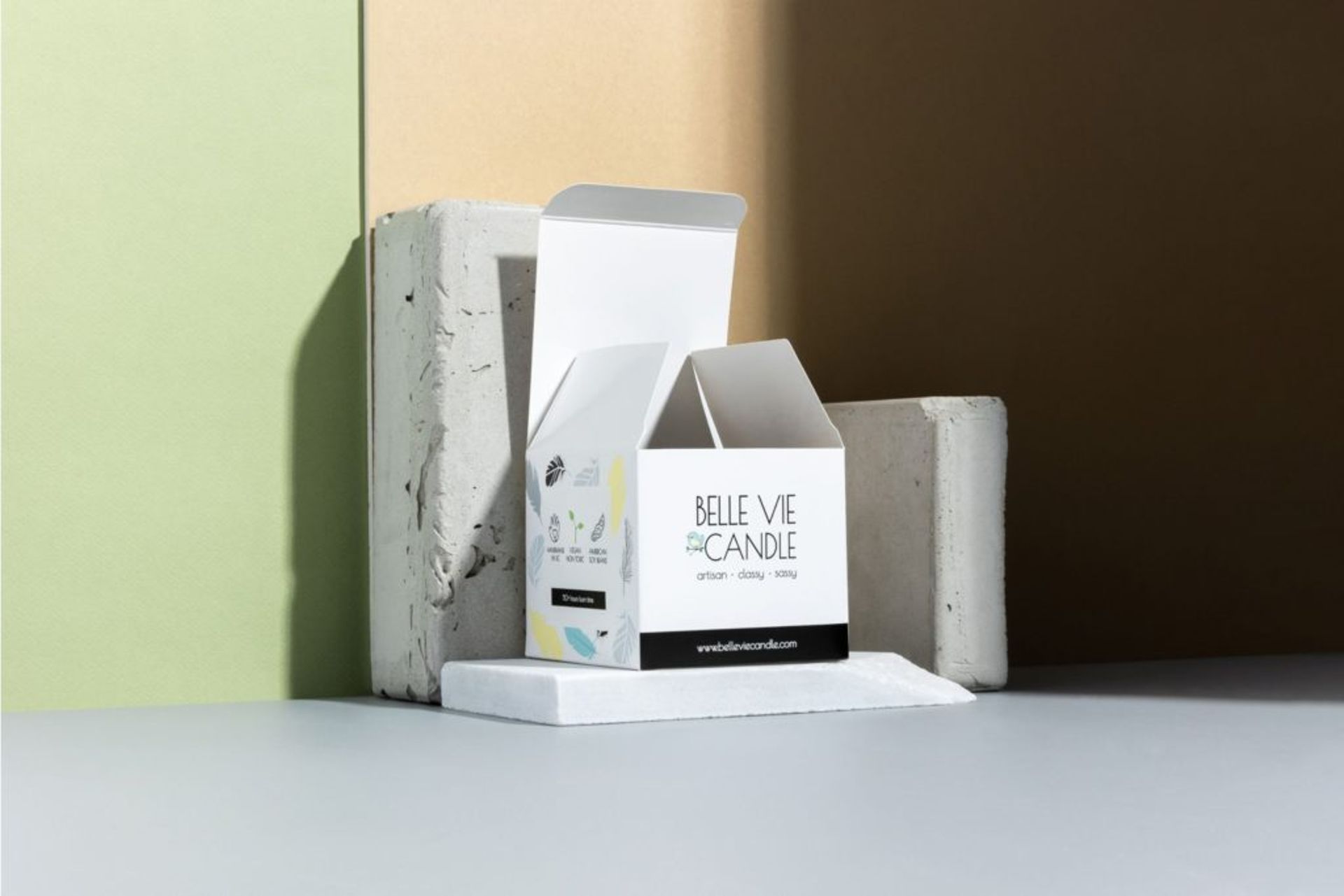 Open Belle Vie Candle folding carton displaying custom printed graphics, resting on concrete blocks against a pastel wall.
