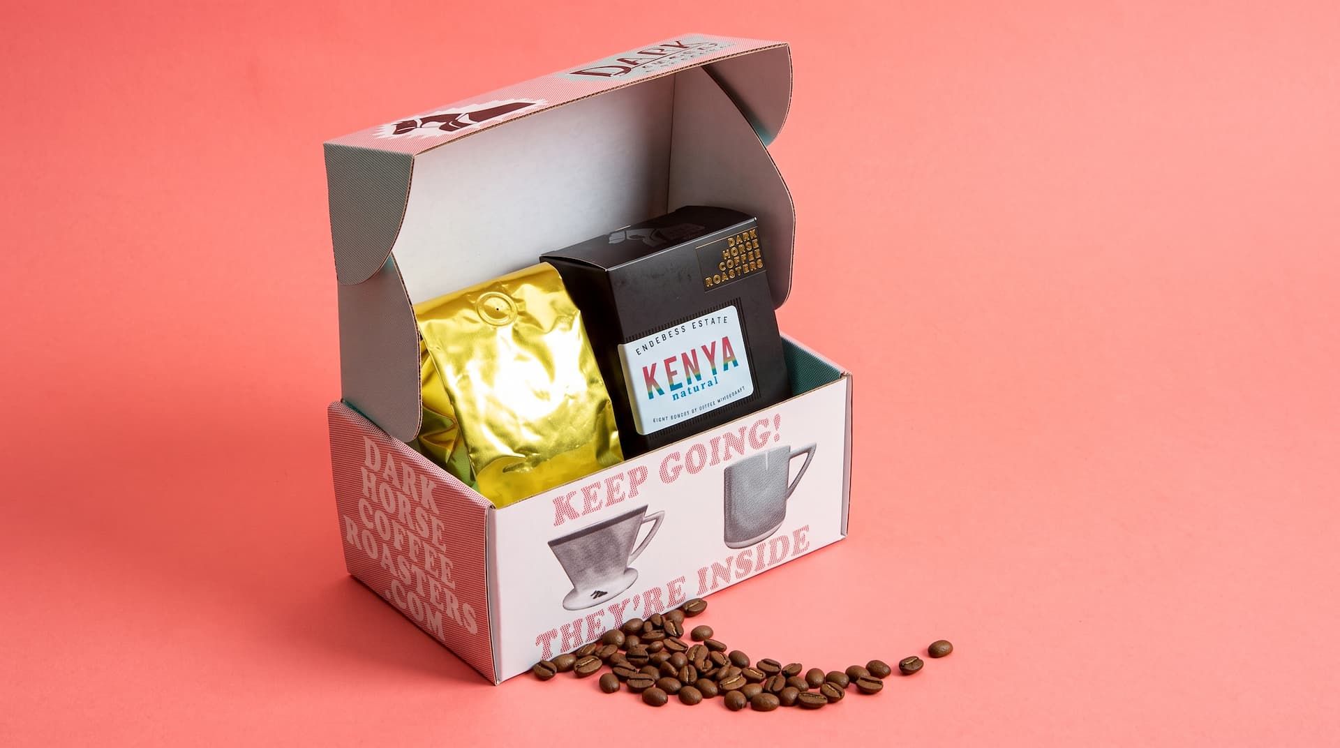 Open Dark Horse coffee box containing a gold foil bag and a black Kenya Natural box, with loose beans on a pink background.