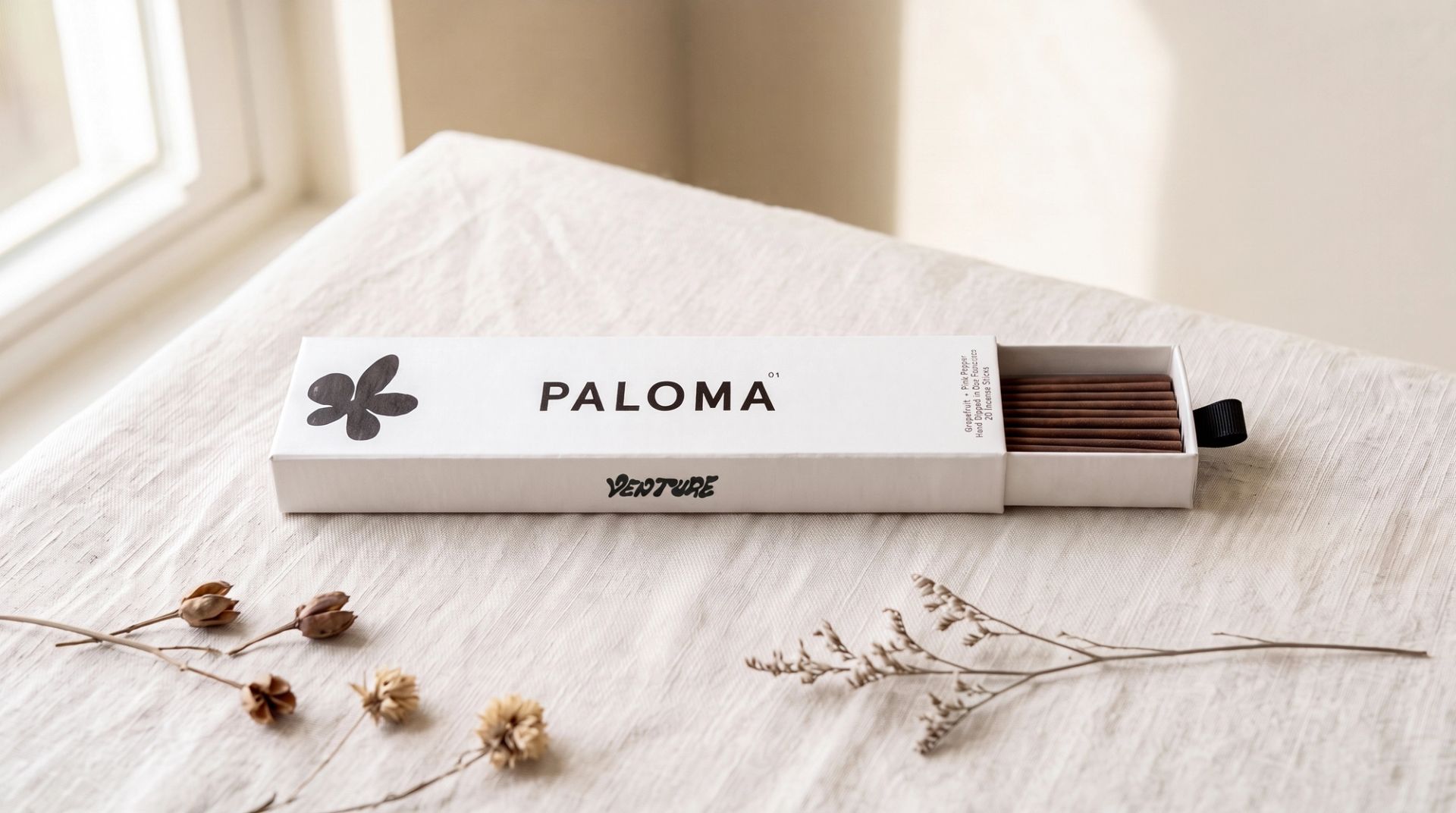 A partially open white drawer box of Venture's Paloma incense resting on a light beige linen cloth.