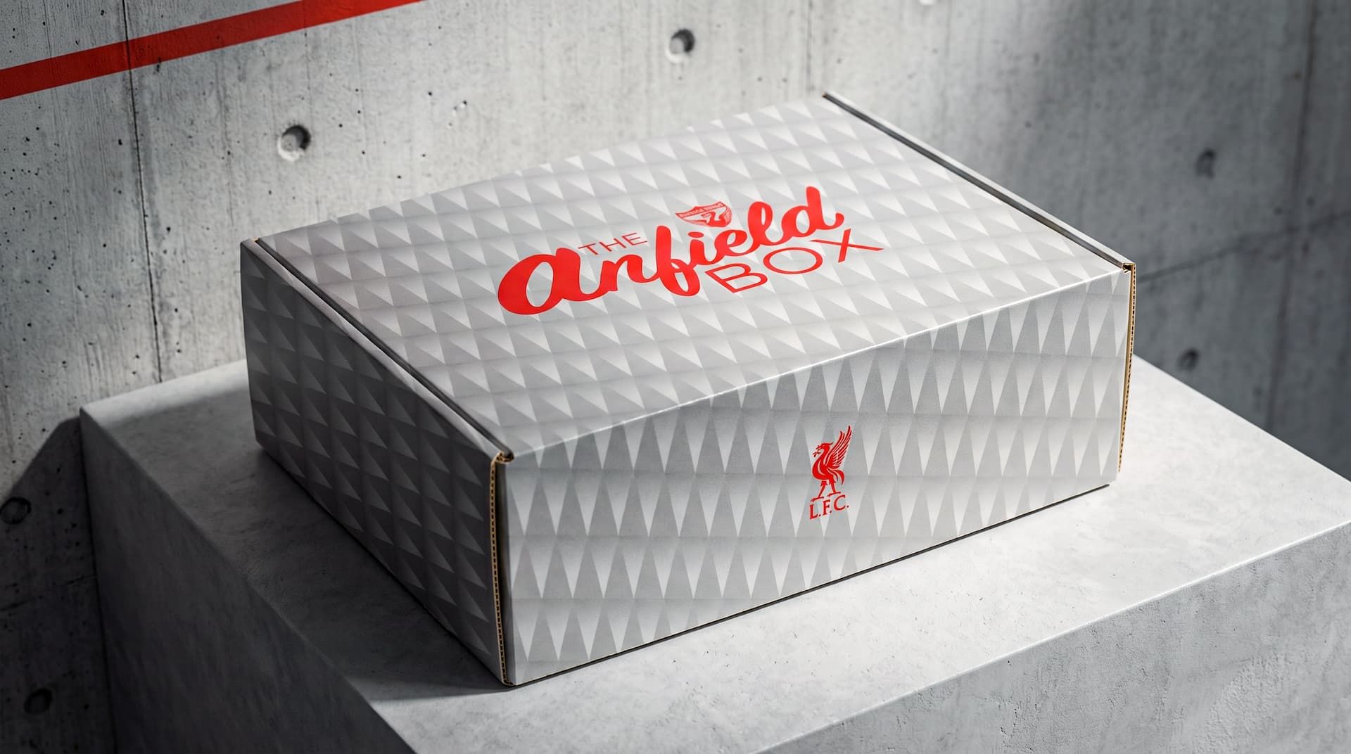 Closed white Anfield Box with a grey geometric pattern and red Liverpool FC logo resting on a concrete block.