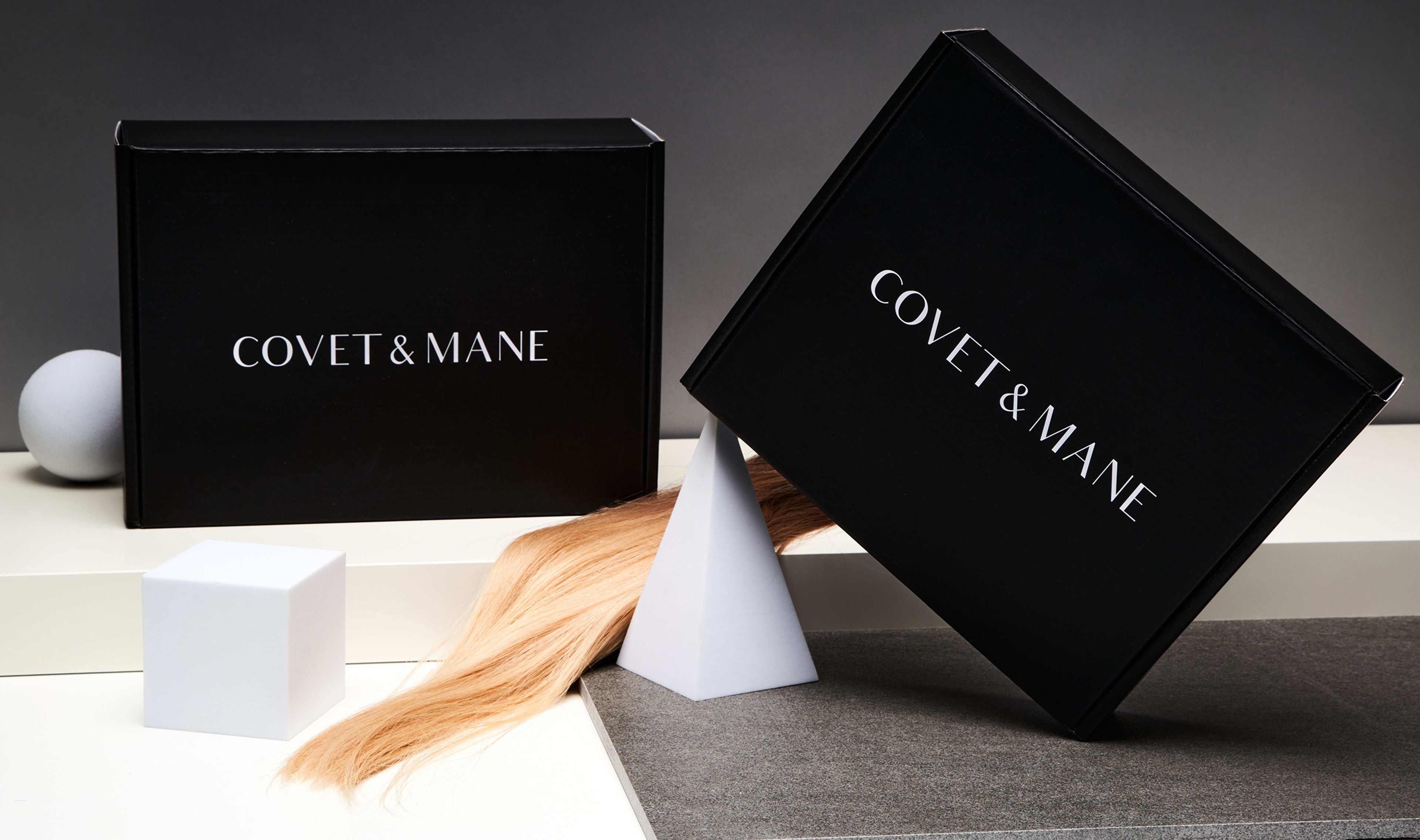 Two sleek black Covet & Mane mailer boxes styled with a blonde hair extension and white geometric shapes.