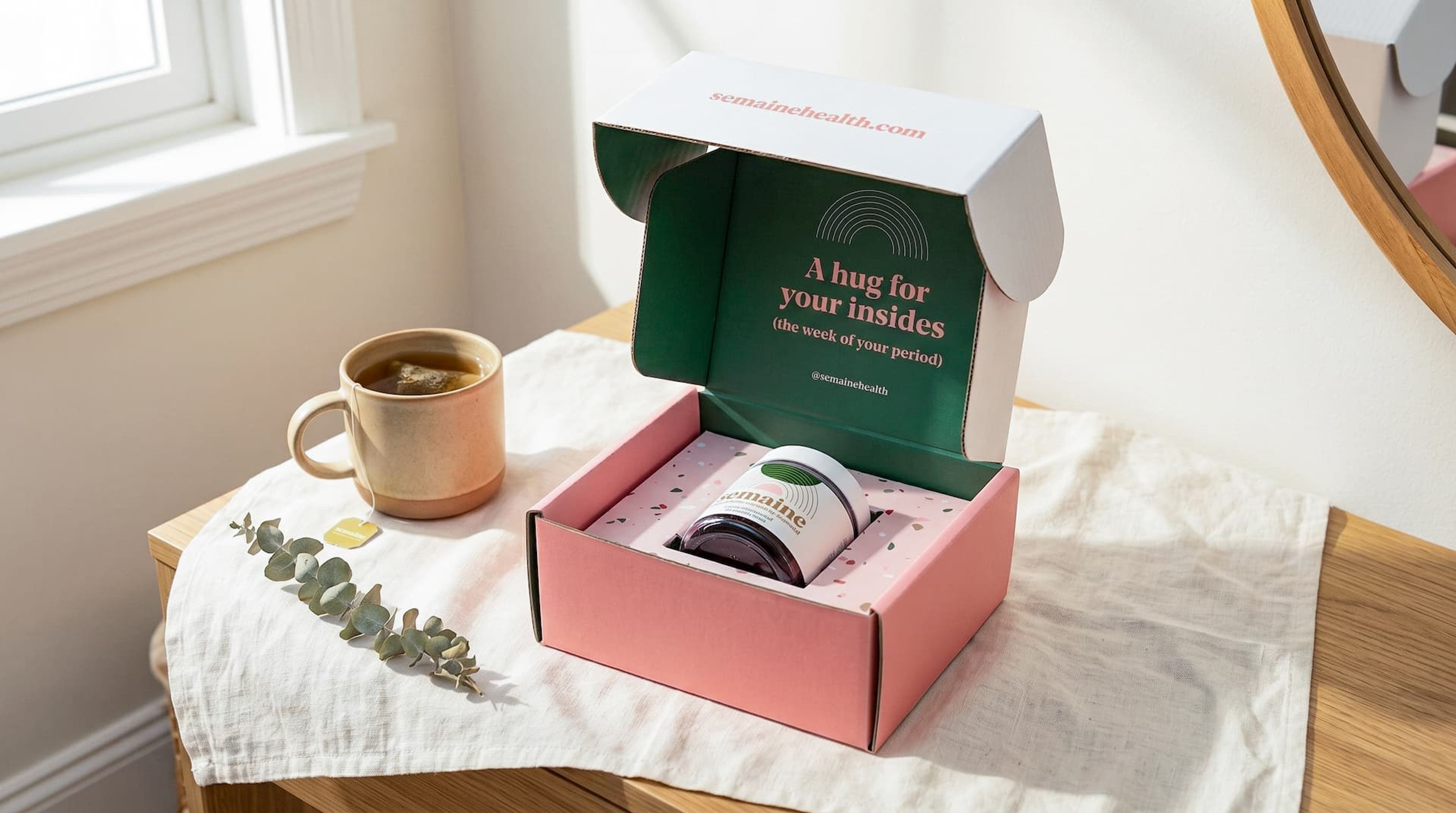 Open Semaine mailer box displaying a supplement jar in a pink insert, set against a cozy aesthetic with tea.