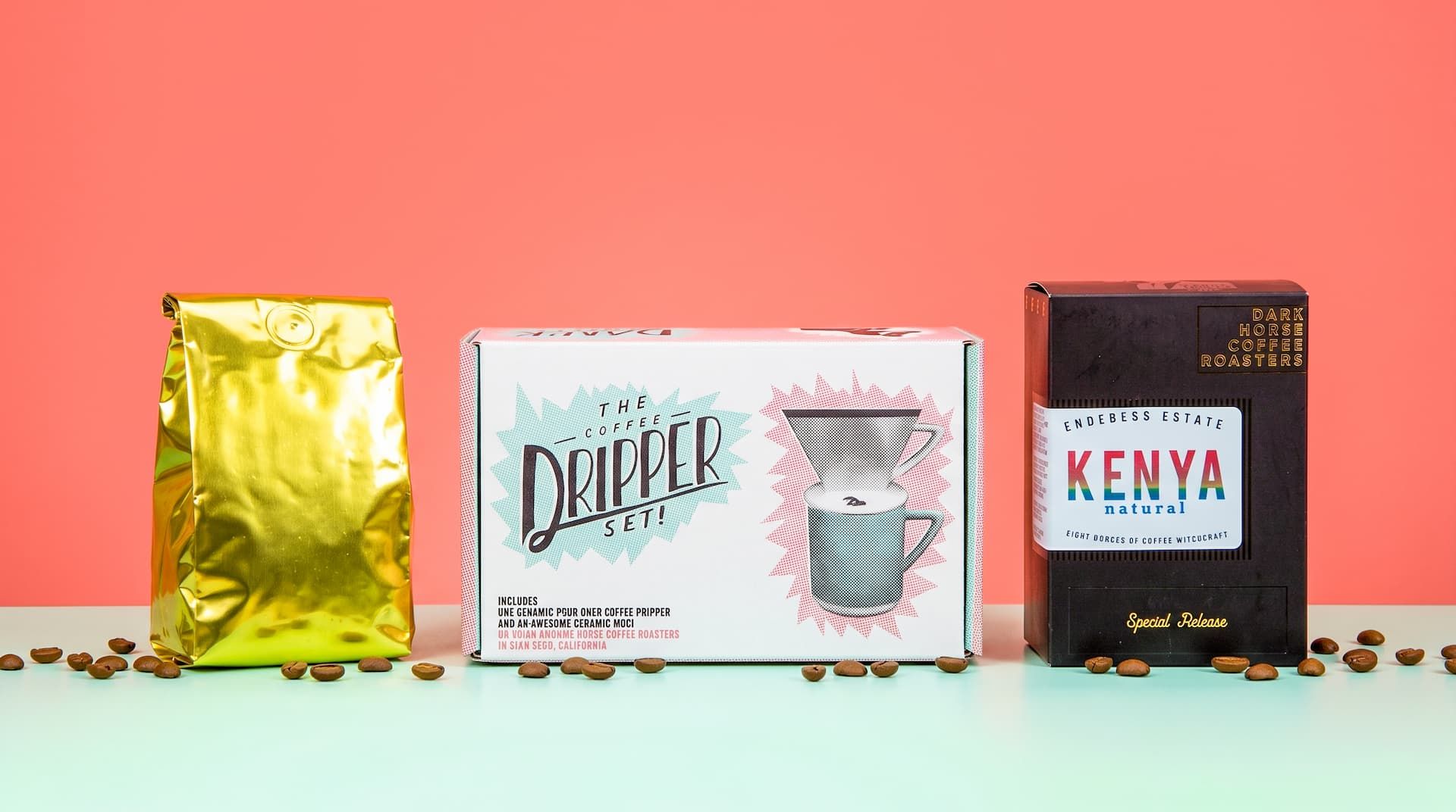 A gold coffee bag, a closed white Coffee Dripper Set box, and a black Kenya Natural coffee box lined up on a mint surface.