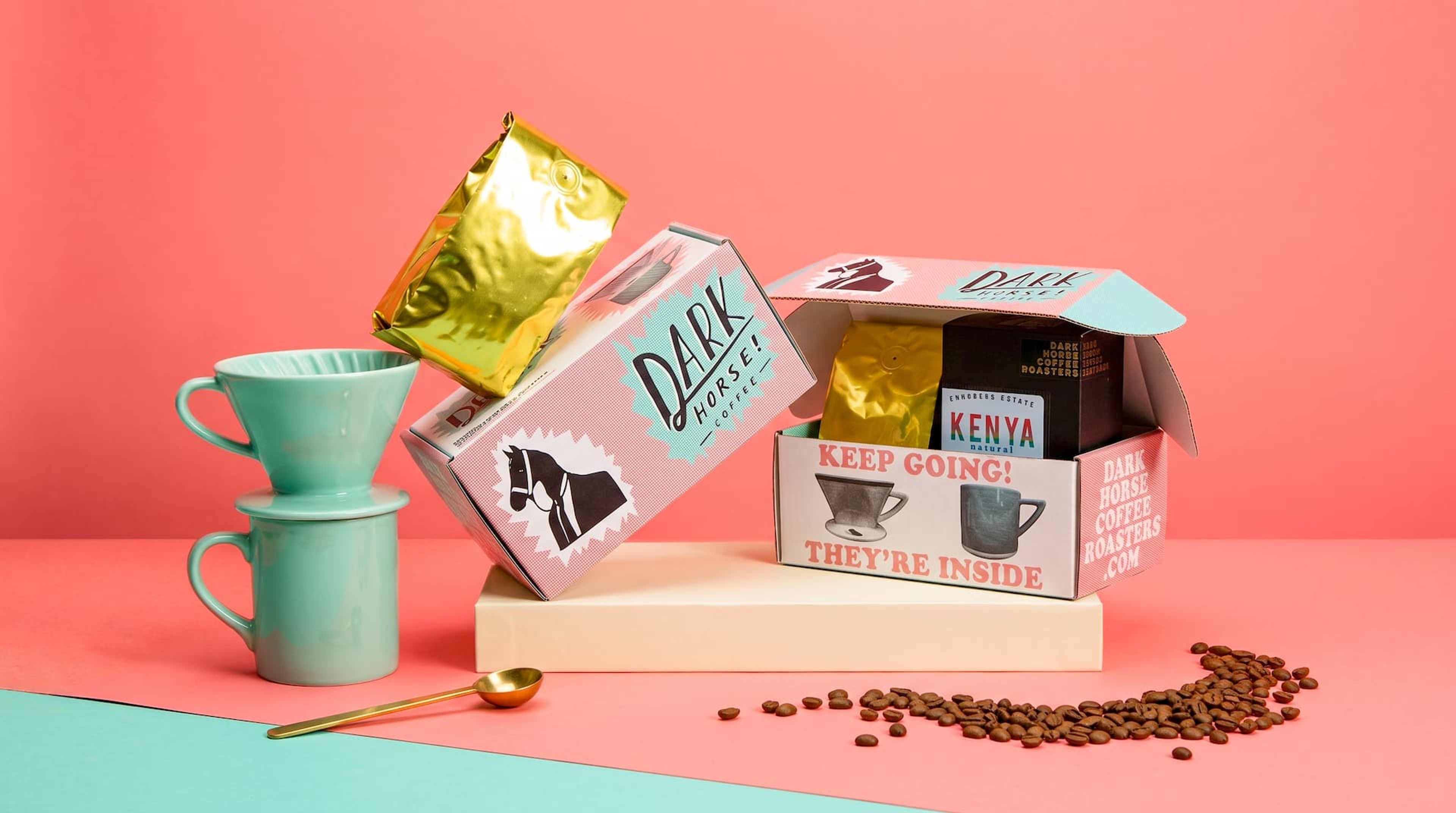A stylized display of Dark Horse Coffee Roasters packaging, including open and closed boxes, a gold bag, and mint mugs.